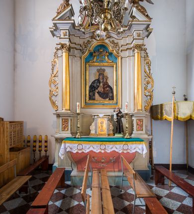 Zdjęcie nr 9: Ołtarz przyścienny, architektoniczny, na cokole. Mensa w typie sarkofagowym; antepedium dekorowane przebitym mieczem gorejącym sercem w wieńcu z róż ujętym kwitnącymi gałązkami. Na mensie tabernakulum na rzucie zbliżonym do prostokąta, na profilowanej podstawie, ujęte spływami wolutowymi. Na licu drzwi w kształcie stojącego prostokąta zamkniętego łukiem półkolistym dekorowane kielichem z hostią, ujęte ustawionymi skośnie pilastrami dźwigającymi pełne belkowanie z wysuniętym gzymsem. Obok tabernakulum stoi figura św. Antoniego Padewskiego. Nastawa jednoosiowa, jednokondygnacyjna ze zwieńczeniem. Oś środkowa flankowana parą kolumn o kapitelach kompozytowych, ustawionych przed licem ołtarza na tle zwielokrotnionych pilastrów. Cokoły kolumn dekorowane płycinami z dekoracją z wici. Podpory dźwigają pełne, wyłamane wielokrotnie belkowanie oraz odpowiadający ich ułożeniu przerwany przyczółek, na którym spoczywa para adorujących aniołów; belkowanie nad częścią środkową ucięte łukowato. W polu środkowym we wnęce w kształcie stojącego prostokąta zamkniętego łukiem nadwieszonym z uskokiem obraz z przedstawieniem Matki Boskiej z Dzieciątkiem w profilowanej ramie z dekoracją płaskorzeźbioną. W ramie ponad obrazem płaskorzeźbiona kompozycja z aniołków trzymających koronę ponad monogramem maryjnym. Powyżej kartusz z napisem „AVE / MARYA”. 
Kondygnację ujmują ażurowe uszaki utworzone z wici roślinnej. Zwieńczenie o kształcie wklęsło-wypukłym, zamknięte od góry łukiem nadwieszonym utworzonym z wolut spiętych muszlą palmetową. Wypełnia je obraz w ramie powtarzającej jego kształt z wizerunkiem św. Cecylii grającej na instrumencie. Zwieńczenie ujmują podobne, ażurowe uszaki. 
Struktura polichromowana na biało ze złoconą ornamentyką oraz detalami architektonicznymi.
