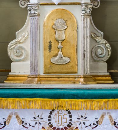 Zdjęcie nr 8: Ołtarz przyścienny, architektoniczny, na cokole. Mensa w typie sarkofagowym; antepedium dekorowane przebitym mieczem gorejącym sercem w wieńcu z róż ujętym kwitnącymi gałązkami. Na mensie tabernakulum na rzucie zbliżonym do prostokąta, na profilowanej podstawie, ujęte spływami wolutowymi. Na licu drzwi w kształcie stojącego prostokąta zamkniętego łukiem półkolistym dekorowane kielichem z hostią, ujęte ustawionymi skośnie pilastrami dźwigającymi pełne belkowanie z wysuniętym gzymsem. Obok tabernakulum stoi figura św. Antoniego Padewskiego. Nastawa jednoosiowa, jednokondygnacyjna ze zwieńczeniem. Oś środkowa flankowana parą kolumn o kapitelach kompozytowych, ustawionych przed licem ołtarza na tle zwielokrotnionych pilastrów. Cokoły kolumn dekorowane płycinami z dekoracją z wici. Podpory dźwigają pełne, wyłamane wielokrotnie belkowanie oraz odpowiadający ich ułożeniu przerwany przyczółek, na którym spoczywa para adorujących aniołów; belkowanie nad częścią środkową ucięte łukowato. W polu środkowym we wnęce w kształcie stojącego prostokąta zamkniętego łukiem nadwieszonym z uskokiem obraz z przedstawieniem Matki Boskiej z Dzieciątkiem w profilowanej ramie z dekoracją płaskorzeźbioną. W ramie ponad obrazem płaskorzeźbiona kompozycja z aniołków trzymających koronę ponad monogramem maryjnym. Powyżej kartusz z napisem „AVE / MARYA”. 
Kondygnację ujmują ażurowe uszaki utworzone z wici roślinnej. Zwieńczenie o kształcie wklęsło-wypukłym, zamknięte od góry łukiem nadwieszonym utworzonym z wolut spiętych muszlą palmetową. Wypełnia je obraz w ramie powtarzającej jego kształt z wizerunkiem św. Cecylii grającej na instrumencie. Zwieńczenie ujmują podobne, ażurowe uszaki. 
Struktura polichromowana na biało ze złoconą ornamentyką oraz detalami architektonicznymi.
