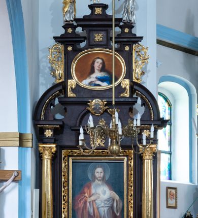 Zdjęcie nr 3: Obraz w kształcie leżącego owalu z fragmentem postaci Matki Boskiej Niepokalanie Poczętej. W centrum kompozycji młoda Maria ukazana w trzech czwartych w prawo, z głową zwróconą do widza, przechyloną nieznacznie do tyłu i rękami złożonymi na piersi. Ma owalną twarz, oczy wzniesione, prosty nos i rozchylone usta; na policzkach delikatny rumieniec. Długie, ciemnoblond włosy spływają jej na plecy i prawe ramię. Jest ubrana w białą suknię i niebieski płaszcz, którego fragment zakrywa jej lewą rękę. Została przedstawiona na tle jasnobrązowego nieba, jej głowę otacza świetlisty nimb. Obraz ujęto złotą, profilowaną ramą. 