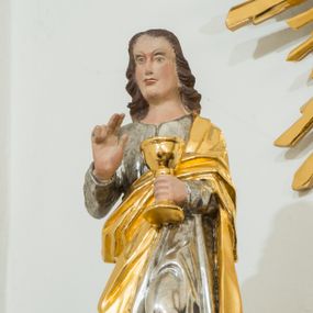 Zdjęcie nr 1: Figura pełna na cokole. Święty Jan ukazany w całej postaci, stojący frontalnie, w kontrapoście, z lewą nogą wysuniętą do przodu. W lewej ręce trzyma kielich, a prawą czyni nad nim gest błogosławieństwa; patrzy przed siebie. Święty ma młodzieńczą, podłużną twarz z asymetrycznie ustawionymi oczami, prostym nosem i wąskimi, silnie zarysowanymi ustami. Długie, ciemnobrązowe włosy zwinięte w pukle opadają mu na plecy. Ubrany jest w srebrną suknię, która fałduje się nad zgiętym kolanem. Na plecy i lewe ramię ma zarzucony złoty płaszcz. Polichromia w odsłoniętych partiach ciała traktowana naturalistycznie.