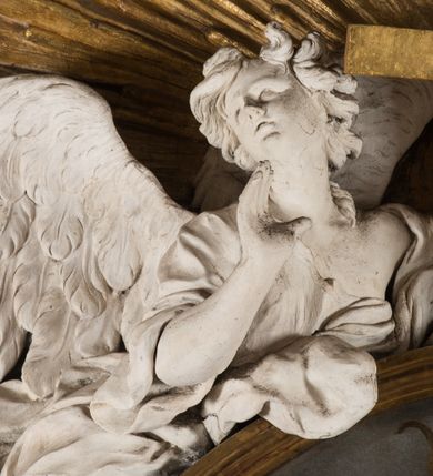Zdjęcie nr 24: Na niskim postumencie o krawędzi przedniej wyciętej linią falistą osadzony ołtarz w kształcie wybrzuszonej górą tumby. Jego antepedium wypełnione marmoryzacją (w technice skaliola) z krzyżującymi się palmami męczeństwa. Po bokach ołtarza dwa ukośnie dostawione postumenty, na których dwie figury aniołów flankujących owalny obraz w złoconej ramie z przedstawieniem męczeństwa św. Sebastiana. Malowidło jest obwiedzione dekoracją sztukatorską w formie obłoków z główkami lub postaciami aniołów, zwieńczone krzyżem i glorią promienistą. Anioły klęczące na postumentach ukazane są w poruszonych pozach, w obficie drapowanych szatach, tworzących grube, mięsiste poły. Anioł po lewej stronie ma głowę zwróconą w kierunku obrazu, a ręce rozkłada na boki, anioł po przeciwnej stronie głowę odwraca w odwrotnym niż obraz kierunku, a jego ręce są uniesione na wysokość klatki piersiowej i skierowane do środka. Nad obrazem anioł po lewej stronie niemalże leży na ramie obrazu, w lewej ręce trzyma krzyż, prawą lekko unosi. Ubrany jest w miękko drapowane szaty, odsłaniające dolną część jego prawej nogi. Duże skrzydła o gęstych piórach rozłożone są niesymetrycznie. Po przeciwnej stronie ukazane putta i główki modelowanych sumarycznie, pulchnych aniołków. Dolne partie wykonane z kamienia, marmoryzowane w jasnych kolorach z czarnym polem antepedium wypełnionym jasnozielonymi palmami męczeństwa. Partie rzeźbiarskie białe, rama obrazu, krzyż i gloria złocone. 

