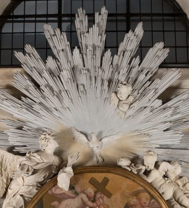 Zdjęcie nr 11: Na niskim postumencie o krawędzi przedniej zarysowanej linią falistą osadzony ołtarz w kształcie tumby, wybrzuszonej w górnej partii. Jego antepedium wypełnione marmoryzacją z owalnym, pustym polem i pękami różnokolorowych kwiatów. Po bokach ołtarza dwa ukośnie dostawione kamienne postumenty, na których dwie figury aniołów flankujących owalny obraz w złoconej ramie z przedstawieniem św. Józefa z Jezusem i grającym na kontrabasie aniołem. Malowidło obwiedzione dekoracją sztukatorską w formie obłoków z główkami lub postaciami aniołów i zwieńczone glorią promienistą z gołębicą Ducha Świętego. Anioły klęczące na postumentach ukazane są w poruszonych pozach, w obficie drapowanych szatach, tworzących grube, mięsiste poły, ze skrzydłami o gęstych piórach. Anioł po lewej stronie jest ukazany frontalnie, klęcząc na chmurze na prawym kolanie, z lewą noga wyprostowaną, z głową w trzech czwartych, zwróconą w swoją prawą stronę. Lewą ręką przytrzymuje ramę obrazu, prawą unosi w geście błogosławieństwa. Anioł po prawej stronie głowę kieruje ku obrazowi, jego ręce są uniesione na wysokości klatki piersiowej, dłoń lewą opuszcza, a prawą unosi. Nad górną częścią obrazu został ukazany anioł w pozycji niemalże leżącej, z rozłożonymi rękami, odziany w bogato drapowane szaty odsłaniające dolną część nogi. Duże skrzydła o gęstych piórach rozłożone są niesymetrycznie. Po przeciwnej stronie leży na chmurach nagie putto wśród modelowanych sumarycznie główek anielskich. Dolne partie wykonane z kamienia inkrustowanego czarnym marmurem i marmoryzacją z różnokolorowymi pękami kwiatów, w jasnych kolorach z czarnym polem antepedium z różnobarwnymi kwiatami, partie rzeźbiarskie białe, rama obrazu złocona, gloria bladoniebieska. 