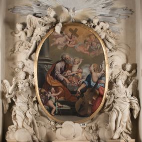 Zdjęcie nr 1: Na niskim postumencie o krawędzi przedniej zarysowanej linią falistą osadzony ołtarz w kształcie tumby, wybrzuszonej w górnej partii. Jego antepedium wypełnione marmoryzacją z owalnym, pustym polem i pękami różnokolorowych kwiatów. Po bokach ołtarza dwa ukośnie dostawione kamienne postumenty, na których dwie figury aniołów flankujących owalny obraz w złoconej ramie z przedstawieniem św. Józefa z Jezusem i grającym na kontrabasie aniołem. Malowidło obwiedzione dekoracją sztukatorską w formie obłoków z główkami lub postaciami aniołów i zwieńczone glorią promienistą z gołębicą Ducha Świętego. Anioły klęczące na postumentach ukazane są w poruszonych pozach, w obficie drapowanych szatach, tworzących grube, mięsiste poły, ze skrzydłami o gęstych piórach. Anioł po lewej stronie jest ukazany frontalnie, klęcząc na chmurze na prawym kolanie, z lewą noga wyprostowaną, z głową w trzech czwartych, zwróconą w swoją prawą stronę. Lewą ręką przytrzymuje ramę obrazu, prawą unosi w geście błogosławieństwa. Anioł po prawej stronie głowę kieruje ku obrazowi, jego ręce są uniesione na wysokości klatki piersiowej, dłoń lewą opuszcza, a prawą unosi. Nad górną częścią obrazu został ukazany anioł w pozycji niemalże leżącej, z rozłożonymi rękami, odziany w bogato drapowane szaty odsłaniające dolną część nogi. Duże skrzydła o gęstych piórach rozłożone są niesymetrycznie. Po przeciwnej stronie leży na chmurach nagie putto wśród modelowanych sumarycznie główek anielskich. Dolne partie wykonane z kamienia inkrustowanego czarnym marmurem i marmoryzacją z różnokolorowymi pękami kwiatów, w jasnych kolorach z czarnym polem antepedium z różnobarwnymi kwiatami, partie rzeźbiarskie białe, rama obrazu złocona, gloria bladoniebieska. 