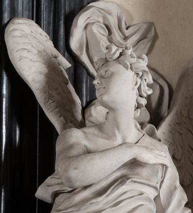 Zdjęcie nr 16: Na niskim postumencie, na rzucie prostokąta z łukiem nadwieszonym od przodu osadzony ołtarz prostopadłościenny. Antepedium marmoryzowane z owalnym polem i rytym przedstawieniem głowy św. Jana Chrzciciela na tacy spoczywającej na postumencie ze skrzyżowanymi szablą i krzyżem oraz banderolą z inskrypcją „ECCE AGNUS DEI”. Zasadniczą część ołtarza stanowi obraz w kształcie stojącego prostokąta w bogato profilowanej, szerokiej ramie, ujętej dwoma aniołami. Obaj stoją na skłębionych obłokach, ukazani frontalnie, w silnym kontrapoście. Ubrani są w przylegające do ich ciał szaty, modelowane swobodnie, silnie drapowane i marszczone. Anioł po lewej głowę zwraca w kierunku obrazu i unosi wysoko złożone w geście modlitwy ręce. Drugi anioł również zwraca się w kierunku obrazu, prawą rękę trzyma na piersi, lewą na wysokości bioder. Obaj mają rozłożyste skrzydła o gęstych piórach. Ramę wieńczy profilowany gzyms wyłamany półkoliście pośrodku z ukośnymi odcinkami na bokach o lekko wklęsłych krawędziach z podwieszonymi pod nie żłobkowanymi impostami, pod którymi unoszące je putta. Nad gzymsem pośrodku siedzi na obłoku z główkami aniołków anioł z rozłożystymi skrzydłami, trzymający w rękach banderolę z napisem „ECCE AGNUS DEI”. Po bokach gzymsu osadzone na nim obłoki z główkami aniołków. Ołtarz z wielobarwną marmoryzacją w dolnej części, czarną ramą i białą dekoracją rzeźbiarską.