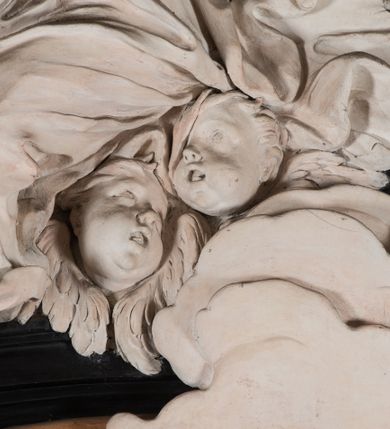 Zdjęcie nr 28: Na niskim postumencie, na rzucie prostokąta z łukiem nadwieszonym od przodu osadzony ołtarz prostopadłościenny. Antepedium marmoryzowane z owalnym polem i rytym przedstawieniem głowy św. Jana Chrzciciela na tacy spoczywającej na postumencie ze skrzyżowanymi szablą i krzyżem oraz banderolą z inskrypcją „ECCE AGNUS DEI”. Zasadniczą część ołtarza stanowi obraz w kształcie stojącego prostokąta w bogato profilowanej, szerokiej ramie, ujętej dwoma aniołami. Obaj stoją na skłębionych obłokach, ukazani frontalnie, w silnym kontrapoście. Ubrani są w przylegające do ich ciał szaty, modelowane swobodnie, silnie drapowane i marszczone. Anioł po lewej głowę zwraca w kierunku obrazu i unosi wysoko złożone w geście modlitwy ręce. Drugi anioł również zwraca się w kierunku obrazu, prawą rękę trzyma na piersi, lewą na wysokości bioder. Obaj mają rozłożyste skrzydła o gęstych piórach. Ramę wieńczy profilowany gzyms wyłamany półkoliście pośrodku z ukośnymi odcinkami na bokach o lekko wklęsłych krawędziach z podwieszonymi pod nie żłobkowanymi impostami, pod którymi unoszące je putta. Nad gzymsem pośrodku siedzi na obłoku z główkami aniołków anioł z rozłożystymi skrzydłami, trzymający w rękach banderolę z napisem „ECCE AGNUS DEI”. Po bokach gzymsu osadzone na nim obłoki z główkami aniołków. Ołtarz z wielobarwną marmoryzacją w dolnej części, czarną ramą i białą dekoracją rzeźbiarską.