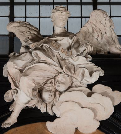 Zdjęcie nr 25: Na niskim postumencie, na rzucie prostokąta z łukiem nadwieszonym od przodu osadzony ołtarz prostopadłościenny. Antepedium marmoryzowane z owalnym polem i rytym przedstawieniem głowy św. Jana Chrzciciela na tacy spoczywającej na postumencie ze skrzyżowanymi szablą i krzyżem oraz banderolą z inskrypcją „ECCE AGNUS DEI”. Zasadniczą część ołtarza stanowi obraz w kształcie stojącego prostokąta w bogato profilowanej, szerokiej ramie, ujętej dwoma aniołami. Obaj stoją na skłębionych obłokach, ukazani frontalnie, w silnym kontrapoście. Ubrani są w przylegające do ich ciał szaty, modelowane swobodnie, silnie drapowane i marszczone. Anioł po lewej głowę zwraca w kierunku obrazu i unosi wysoko złożone w geście modlitwy ręce. Drugi anioł również zwraca się w kierunku obrazu, prawą rękę trzyma na piersi, lewą na wysokości bioder. Obaj mają rozłożyste skrzydła o gęstych piórach. Ramę wieńczy profilowany gzyms wyłamany półkoliście pośrodku z ukośnymi odcinkami na bokach o lekko wklęsłych krawędziach z podwieszonymi pod nie żłobkowanymi impostami, pod którymi unoszące je putta. Nad gzymsem pośrodku siedzi na obłoku z główkami aniołków anioł z rozłożystymi skrzydłami, trzymający w rękach banderolę z napisem „ECCE AGNUS DEI”. Po bokach gzymsu osadzone na nim obłoki z główkami aniołków. Ołtarz z wielobarwną marmoryzacją w dolnej części, czarną ramą i białą dekoracją rzeźbiarską.