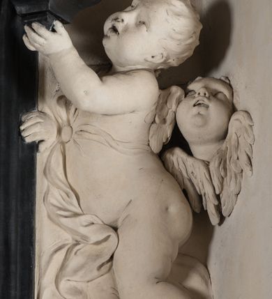 Zdjęcie nr 31: Na niskim postumencie, na rzucie prostokąta z łukiem nadwieszonym od przodu osadzony ołtarz prostopadłościenny. Antepedium marmoryzowane z owalnym polem i rytym przedstawieniem głowy św. Jana Chrzciciela na tacy spoczywającej na postumencie ze skrzyżowanymi szablą i krzyżem oraz banderolą z inskrypcją „ECCE AGNUS DEI”. Zasadniczą część ołtarza stanowi obraz w kształcie stojącego prostokąta w bogato profilowanej, szerokiej ramie, ujętej dwoma aniołami. Obaj stoją na skłębionych obłokach, ukazani frontalnie, w silnym kontrapoście. Ubrani są w przylegające do ich ciał szaty, modelowane swobodnie, silnie drapowane i marszczone. Anioł po lewej głowę zwraca w kierunku obrazu i unosi wysoko złożone w geście modlitwy ręce. Drugi anioł również zwraca się w kierunku obrazu, prawą rękę trzyma na piersi, lewą na wysokości bioder. Obaj mają rozłożyste skrzydła o gęstych piórach. Ramę wieńczy profilowany gzyms wyłamany półkoliście pośrodku z ukośnymi odcinkami na bokach o lekko wklęsłych krawędziach z podwieszonymi pod nie żłobkowanymi impostami, pod którymi unoszące je putta. Nad gzymsem pośrodku siedzi na obłoku z główkami aniołków anioł z rozłożystymi skrzydłami, trzymający w rękach banderolę z napisem „ECCE AGNUS DEI”. Po bokach gzymsu osadzone na nim obłoki z główkami aniołków. Ołtarz z wielobarwną marmoryzacją w dolnej części, czarną ramą i białą dekoracją rzeźbiarską.