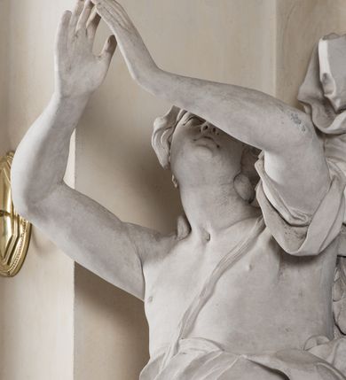 Zdjęcie nr 23: Na niskim postumencie, na rzucie prostokąta z łukiem nadwieszonym od przodu osadzony ołtarz prostopadłościenny. Antepedium marmoryzowane z owalnym polem i rytym przedstawieniem głowy św. Jana Chrzciciela na tacy spoczywającej na postumencie ze skrzyżowanymi szablą i krzyżem oraz banderolą z inskrypcją „ECCE AGNUS DEI”. Zasadniczą część ołtarza stanowi obraz w kształcie stojącego prostokąta w bogato profilowanej, szerokiej ramie, ujętej dwoma aniołami. Obaj stoją na skłębionych obłokach, ukazani frontalnie, w silnym kontrapoście. Ubrani są w przylegające do ich ciał szaty, modelowane swobodnie, silnie drapowane i marszczone. Anioł po lewej głowę zwraca w kierunku obrazu i unosi wysoko złożone w geście modlitwy ręce. Drugi anioł również zwraca się w kierunku obrazu, prawą rękę trzyma na piersi, lewą na wysokości bioder. Obaj mają rozłożyste skrzydła o gęstych piórach. Ramę wieńczy profilowany gzyms wyłamany półkoliście pośrodku z ukośnymi odcinkami na bokach o lekko wklęsłych krawędziach z podwieszonymi pod nie żłobkowanymi impostami, pod którymi unoszące je putta. Nad gzymsem pośrodku siedzi na obłoku z główkami aniołków anioł z rozłożystymi skrzydłami, trzymający w rękach banderolę z napisem „ECCE AGNUS DEI”. Po bokach gzymsu osadzone na nim obłoki z główkami aniołków. Ołtarz z wielobarwną marmoryzacją w dolnej części, czarną ramą i białą dekoracją rzeźbiarską.