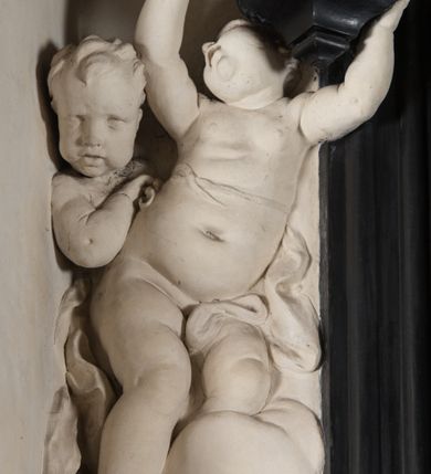 Zdjęcie nr 29: Na niskim postumencie, na rzucie prostokąta z łukiem nadwieszonym od przodu osadzony ołtarz prostopadłościenny. Antepedium marmoryzowane z owalnym polem i rytym przedstawieniem głowy św. Jana Chrzciciela na tacy spoczywającej na postumencie ze skrzyżowanymi szablą i krzyżem oraz banderolą z inskrypcją „ECCE AGNUS DEI”. Zasadniczą część ołtarza stanowi obraz w kształcie stojącego prostokąta w bogato profilowanej, szerokiej ramie, ujętej dwoma aniołami. Obaj stoją na skłębionych obłokach, ukazani frontalnie, w silnym kontrapoście. Ubrani są w przylegające do ich ciał szaty, modelowane swobodnie, silnie drapowane i marszczone. Anioł po lewej głowę zwraca w kierunku obrazu i unosi wysoko złożone w geście modlitwy ręce. Drugi anioł również zwraca się w kierunku obrazu, prawą rękę trzyma na piersi, lewą na wysokości bioder. Obaj mają rozłożyste skrzydła o gęstych piórach. Ramę wieńczy profilowany gzyms wyłamany półkoliście pośrodku z ukośnymi odcinkami na bokach o lekko wklęsłych krawędziach z podwieszonymi pod nie żłobkowanymi impostami, pod którymi unoszące je putta. Nad gzymsem pośrodku siedzi na obłoku z główkami aniołków anioł z rozłożystymi skrzydłami, trzymający w rękach banderolę z napisem „ECCE AGNUS DEI”. Po bokach gzymsu osadzone na nim obłoki z główkami aniołków. Ołtarz z wielobarwną marmoryzacją w dolnej części, czarną ramą i białą dekoracją rzeźbiarską.