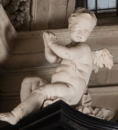 Zdjęcie nr 48: Na niskim postumencie, na rzucie prostokąta z łukiem nadwieszonym od przodu, prostopadłościenny ołtarz z antepedium ujętym szerokimi lizenami z romboidalnymi polami wypełnionymi drobnymi kwiatami, z owalnym polem pośrodku z podłużnymi palmami męczeństwa i bukietami kwiatów wokół. Nad ołtarzem nastawa z obrazem w kształcie stojącego prostokąta z przedstawieniem św. Piotra uwalnianego przez anioła z okowów. Ołtarz jest ujęty ukośnie dostawionymi postumentami z figurami dwóch aniołów flankujących obraz. Anioły ukazane w poruszonych pozach. Lewy stoi w silnym kontrapoście, z prawą nogą opartą na chmurze, z ciałem skierowanym ku środkowi osi ołtarza, z głową odwróconą w kierunku przeciwnym i wysuniętymi przed siebie rękami złożonymi do modlitwy. Jego twarz jest modelowana łagodnie, nos ma długi, usta rozwarte, a włosy skręcone, krótkie. Ubrany w obficie drapowany płaszcz, którego poły układają się w miękkie fałdy, dołem przechodzące między łydkami. Skrzydła ma rozłożyste, modelowane niesymetrycznie, gęsto upierzone. Drugi anioł klęczy na lewej nodze, wspartej na chmurze, zwrócony jest w kierunku obrazu, z prawą ręką przed sobą, a lewą odrzuconą do tyłu. Twarz ma pociągłą, nos wydatny, włosy krótkie, skręcone. Ubrany w długą suknię, drapowaną obficie, odsłaniającą lewe przedramię. Skrzydła rozłożyste, gęsto upierzone. Górna część ramy obrazu z ukośnie wyłamanym gzymsem z podwieszonymi pod nim impostami, podtrzymywanymi przez wyłaniające się z chmur anioły. Gzyms nad obrazem wyłamuje się półkoliście, na nim pośrodku leży anioł trzymający w lewej ręce banderolę ze złoconymi literami nietworzącymi logicznej całości, a prawą ręką wskazujący w kierunku wnętrza kaplicy. U jego boku skłębione chmury z trzema uskrzydlonymi główkami aniołków. Nad bocznymi partiami gzymsu siedzą uskrzydlone, nagie, pulchne aniołki, jeden z rękami złożonymi w geście modlitwy, drugi z rękami uniesionymi i rozłożonymi. Marmoryzacja utrzymana w kolorach brązów, rama i zwieńczenie czarne, dekoracja rzeźbiarska biała. 