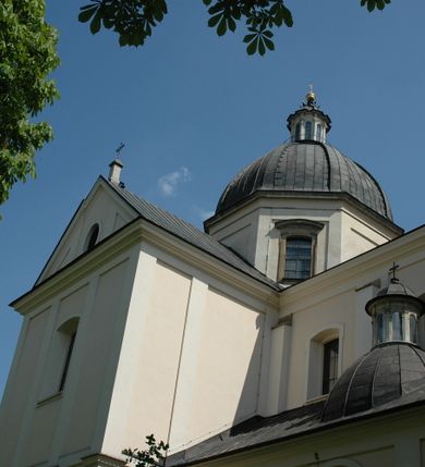 Zdjęcie nr 57: Kościół jest murowany z cegły, z użyciem ciosu kamiennego w partii cokołu i jako okładziny, tynkowany, z kryptami odpowiadającymi rzutowi. Założony jest na rzucie krzyża łacińskiego, z czteroprzęsłową nawą ujętą kaplicami, trójprzęsłowym prezbiterium zamknięty prosto, półtoraprzęsłowymi ramionami nawy poprzecznej, wysuniętymi poza korpus, zamknięte prosto i z kopułą na skrzyżowaniu naw. Przęsło fasady jest ujęte dwiema lokalnościami i dwiema wysuniętymi poza obręb korpusu wieżami z okrągłymi klatkami schodowymi z drewnianymi kręconymi schodami prowadzącymi do pomieszczeń nad lokalnościami. Do prezbiterium przylegają od południowego wschodu zakrystia, od północnego zachodu skarbiec, z składzikami na piętrze. 
Nawa jest artykułowa za pomocą pilastrów kompozytowych, zdwojonych w prezbiterium, transepcie i nawie głównej, zwielokrotniony w krzyżu kościoła, dźwigających wydatne belkowanie. Ściany kaplic są artykułowane za pomocą płytkich, opilastrowanych arkad; mury tarczowe kaplic wydzielone za pomocą gzymsu przełamującego się w narożnikach. Nawa i prezbiterium są sklepione kolebkami na gurtach z lunetami, transept sklepieniem kolebkowym na gurtach, kaplice pseudokopułami na pendentywach (w kaplicy Matki Boskiej i św. Katarzyny kopuły na rzucie elipsy z latarniami), zakrystia i skarbiec sklepieniem krzyżowo-kolebkowo, a przedsionki – nieckowym z lustrem. Okna nawy głównej i prezbiterium w profilowanych obramieniach, prostokątne, zamknięte łukiem segmentowym, okna kaplic są półkoliste. Bęben kopuły rozczłonkowany parami pilastrów kompozytowych, a między nimi rozlokowane naprzemian półkoliście zamknięte nisze i prostokątne okna. Do kościoła prowadzą drzwi wejściowe i para drzwi bocznych, z prezbiterium drzwi wejściowe do skarbca i zakrystii, z zakrystii na dziedziniec przy kościele. 
Fasada poprzedzona schodami, dwukondygnacyjna, dwuwieżowa, w dolnej kondygnacji siedmioosiowa, w górnej trójosiowa z dwiema wyodrębnionymi wieżami. Dolna kondygnacja rozczłonkowana zwojonymi pilastrami i parami kolumn flankujących oś środkową, o kapitelach kompozytowych, podtrzymujących wyłamujące się nad nimi belkowanie z wydatnym gzymsem i attyką, ponad belkowaniem w osi środkowej przerwany przyczółek. Górną kondygnację ujmują pary pilastrów ze stojącymi na ich tle wazonami, dźwigające wyłamujące się nad nimi belkowanie, w części środkowej zwieńczone przyczółkiem, w wieżach – miedzianymi hełmami. 
W części środkowej dolnej kondygnacji znajduje się zamknięta półkoliście wnęka z portalem, ujętym ukośnie dostawionymi pilastrami z konsolami podtrzymującymi naczółki i z tablicą z wklęsłymi bokami, zwieńczoną gzymsem w kształcie łuku nadwieszonego; ponad tablicą znajduje się półkoliste okno. Nad drzwiami bocznymi płaskorzeźbione postacie klęczących aniołów i kwadratowe okna, w wieżach wnęki z figurami św. Bernarda (po lewej) i św. Jana Kantego (po prawej). W części środkowej drugiej kondygnacji umieszczone jest prostokątne okno zamknięte łukiem segmentowym i zwieńczone przerwanym przyczółkiem. W polach bocznych nisze z figurami św. Kazimierza (po lewej) i św. Floriana (po prawej). Ściany boczne wzmocnione szkarpami, podzielone lizenami i pilastrami toskańskimi w dolnej kondygnacji prezbiterium oraz południowo wschodniej i północno zachodniej ścianie transeptu. Prezbiterium i ramiona transeptu zamknięte trójkątnymi szczytami z owalnymi oknami. Tambur kopuły rozczłonkowany lizenami, z oknami zamkniętymi łukami segmentowymi, w profilowanych obramieniach; ośmiopolową kopułę krytą blachą wieńczy latarnia opięta półkolumnami, pomiędzy którymi znajdują się wąskie okna zamknięte półkoliście. Nawę, prezbiterium i transept nakrywa dach siodłowy, nad pozostałymi pomieszczeniami dachy siodłowe, z wyjątkiem środkowych kaplic, w których kopułki wtopione zostały w dach i zwieńczone latarniami.  
