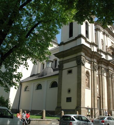 Zdjęcie nr 13: Kościół jest murowany z cegły, z użyciem ciosu kamiennego w partii cokołu i jako okładziny, tynkowany, z kryptami odpowiadającymi rzutowi. Założony jest na rzucie krzyża łacińskiego, z czteroprzęsłową nawą ujętą kaplicami, trójprzęsłowym prezbiterium zamknięty prosto, półtoraprzęsłowymi ramionami nawy poprzecznej, wysuniętymi poza korpus, zamknięte prosto i z kopułą na skrzyżowaniu naw. Przęsło fasady jest ujęte dwiema lokalnościami i dwiema wysuniętymi poza obręb korpusu wieżami z okrągłymi klatkami schodowymi z drewnianymi kręconymi schodami prowadzącymi do pomieszczeń nad lokalnościami. Do prezbiterium przylegają od południowego wschodu zakrystia, od północnego zachodu skarbiec, z składzikami na piętrze. 
Nawa jest artykułowa za pomocą pilastrów kompozytowych, zdwojonych w prezbiterium, transepcie i nawie głównej, zwielokrotniony w krzyżu kościoła, dźwigających wydatne belkowanie. Ściany kaplic są artykułowane za pomocą płytkich, opilastrowanych arkad; mury tarczowe kaplic wydzielone za pomocą gzymsu przełamującego się w narożnikach. Nawa i prezbiterium są sklepione kolebkami na gurtach z lunetami, transept sklepieniem kolebkowym na gurtach, kaplice pseudokopułami na pendentywach (w kaplicy Matki Boskiej i św. Katarzyny kopuły na rzucie elipsy z latarniami), zakrystia i skarbiec sklepieniem krzyżowo-kolebkowo, a przedsionki – nieckowym z lustrem. Okna nawy głównej i prezbiterium w profilowanych obramieniach, prostokątne, zamknięte łukiem segmentowym, okna kaplic są półkoliste. Bęben kopuły rozczłonkowany parami pilastrów kompozytowych, a między nimi rozlokowane naprzemian półkoliście zamknięte nisze i prostokątne okna. Do kościoła prowadzą drzwi wejściowe i para drzwi bocznych, z prezbiterium drzwi wejściowe do skarbca i zakrystii, z zakrystii na dziedziniec przy kościele. 
Fasada poprzedzona schodami, dwukondygnacyjna, dwuwieżowa, w dolnej kondygnacji siedmioosiowa, w górnej trójosiowa z dwiema wyodrębnionymi wieżami. Dolna kondygnacja rozczłonkowana zwojonymi pilastrami i parami kolumn flankujących oś środkową, o kapitelach kompozytowych, podtrzymujących wyłamujące się nad nimi belkowanie z wydatnym gzymsem i attyką, ponad belkowaniem w osi środkowej przerwany przyczółek. Górną kondygnację ujmują pary pilastrów ze stojącymi na ich tle wazonami, dźwigające wyłamujące się nad nimi belkowanie, w części środkowej zwieńczone przyczółkiem, w wieżach – miedzianymi hełmami. 
W części środkowej dolnej kondygnacji znajduje się zamknięta półkoliście wnęka z portalem, ujętym ukośnie dostawionymi pilastrami z konsolami podtrzymującymi naczółki i z tablicą z wklęsłymi bokami, zwieńczoną gzymsem w kształcie łuku nadwieszonego; ponad tablicą znajduje się półkoliste okno. Nad drzwiami bocznymi płaskorzeźbione postacie klęczących aniołów i kwadratowe okna, w wieżach wnęki z figurami św. Bernarda (po lewej) i św. Jana Kantego (po prawej). W części środkowej drugiej kondygnacji umieszczone jest prostokątne okno zamknięte łukiem segmentowym i zwieńczone przerwanym przyczółkiem. W polach bocznych nisze z figurami św. Kazimierza (po lewej) i św. Floriana (po prawej). Ściany boczne wzmocnione szkarpami, podzielone lizenami i pilastrami toskańskimi w dolnej kondygnacji prezbiterium oraz południowo wschodniej i północno zachodniej ścianie transeptu. Prezbiterium i ramiona transeptu zamknięte trójkątnymi szczytami z owalnymi oknami. Tambur kopuły rozczłonkowany lizenami, z oknami zamkniętymi łukami segmentowymi, w profilowanych obramieniach; ośmiopolową kopułę krytą blachą wieńczy latarnia opięta półkolumnami, pomiędzy którymi znajdują się wąskie okna zamknięte półkoliście. Nawę, prezbiterium i transept nakrywa dach siodłowy, nad pozostałymi pomieszczeniami dachy siodłowe, z wyjątkiem środkowych kaplic, w których kopułki wtopione zostały w dach i zwieńczone latarniami.  
