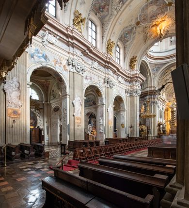 Zdjęcie nr 86: Kościół jest murowany z cegły, z użyciem ciosu kamiennego w partii cokołu i jako okładziny, tynkowany, z kryptami odpowiadającymi rzutowi. Założony jest na rzucie krzyża łacińskiego, z czteroprzęsłową nawą ujętą kaplicami, trójprzęsłowym prezbiterium zamknięty prosto, półtoraprzęsłowymi ramionami nawy poprzecznej, wysuniętymi poza korpus, zamknięte prosto i z kopułą na skrzyżowaniu naw. Przęsło fasady jest ujęte dwiema lokalnościami i dwiema wysuniętymi poza obręb korpusu wieżami z okrągłymi klatkami schodowymi z drewnianymi kręconymi schodami prowadzącymi do pomieszczeń nad lokalnościami. Do prezbiterium przylegają od południowego wschodu zakrystia, od północnego zachodu skarbiec, z składzikami na piętrze. 
Nawa jest artykułowa za pomocą pilastrów kompozytowych, zdwojonych w prezbiterium, transepcie i nawie głównej, zwielokrotniony w krzyżu kościoła, dźwigających wydatne belkowanie. Ściany kaplic są artykułowane za pomocą płytkich, opilastrowanych arkad; mury tarczowe kaplic wydzielone za pomocą gzymsu przełamującego się w narożnikach. Nawa i prezbiterium są sklepione kolebkami na gurtach z lunetami, transept sklepieniem kolebkowym na gurtach, kaplice pseudokopułami na pendentywach (w kaplicy Matki Boskiej i św. Katarzyny kopuły na rzucie elipsy z latarniami), zakrystia i skarbiec sklepieniem krzyżowo-kolebkowo, a przedsionki – nieckowym z lustrem. Okna nawy głównej i prezbiterium w profilowanych obramieniach, prostokątne, zamknięte łukiem segmentowym, okna kaplic są półkoliste. Bęben kopuły rozczłonkowany parami pilastrów kompozytowych, a między nimi rozlokowane naprzemian półkoliście zamknięte nisze i prostokątne okna. Do kościoła prowadzą drzwi wejściowe i para drzwi bocznych, z prezbiterium drzwi wejściowe do skarbca i zakrystii, z zakrystii na dziedziniec przy kościele. 
Fasada poprzedzona schodami, dwukondygnacyjna, dwuwieżowa, w dolnej kondygnacji siedmioosiowa, w górnej trójosiowa z dwiema wyodrębnionymi wieżami. Dolna kondygnacja rozczłonkowana zwojonymi pilastrami i parami kolumn flankujących oś środkową, o kapitelach kompozytowych, podtrzymujących wyłamujące się nad nimi belkowanie z wydatnym gzymsem i attyką, ponad belkowaniem w osi środkowej przerwany przyczółek. Górną kondygnację ujmują pary pilastrów ze stojącymi na ich tle wazonami, dźwigające wyłamujące się nad nimi belkowanie, w części środkowej zwieńczone przyczółkiem, w wieżach – miedzianymi hełmami. 
W części środkowej dolnej kondygnacji znajduje się zamknięta półkoliście wnęka z portalem, ujętym ukośnie dostawionymi pilastrami z konsolami podtrzymującymi naczółki i z tablicą z wklęsłymi bokami, zwieńczoną gzymsem w kształcie łuku nadwieszonego; ponad tablicą znajduje się półkoliste okno. Nad drzwiami bocznymi płaskorzeźbione postacie klęczących aniołów i kwadratowe okna, w wieżach wnęki z figurami św. Bernarda (po lewej) i św. Jana Kantego (po prawej). W części środkowej drugiej kondygnacji umieszczone jest prostokątne okno zamknięte łukiem segmentowym i zwieńczone przerwanym przyczółkiem. W polach bocznych nisze z figurami św. Kazimierza (po lewej) i św. Floriana (po prawej). Ściany boczne wzmocnione szkarpami, podzielone lizenami i pilastrami toskańskimi w dolnej kondygnacji prezbiterium oraz południowo wschodniej i północno zachodniej ścianie transeptu. Prezbiterium i ramiona transeptu zamknięte trójkątnymi szczytami z owalnymi oknami. Tambur kopuły rozczłonkowany lizenami, z oknami zamkniętymi łukami segmentowymi, w profilowanych obramieniach; ośmiopolową kopułę krytą blachą wieńczy latarnia opięta półkolumnami, pomiędzy którymi znajdują się wąskie okna zamknięte półkoliście. Nawę, prezbiterium i transept nakrywa dach siodłowy, nad pozostałymi pomieszczeniami dachy siodłowe, z wyjątkiem środkowych kaplic, w których kopułki wtopione zostały w dach i zwieńczone latarniami.  
