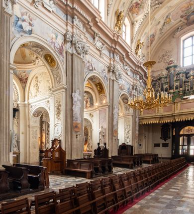 Zdjęcie nr 14: Kościół jest murowany z cegły, z użyciem ciosu kamiennego w partii cokołu i jako okładziny, tynkowany, z kryptami odpowiadającymi rzutowi. Założony jest na rzucie krzyża łacińskiego, z czteroprzęsłową nawą ujętą kaplicami, trójprzęsłowym prezbiterium zamknięty prosto, półtoraprzęsłowymi ramionami nawy poprzecznej, wysuniętymi poza korpus, zamknięte prosto i z kopułą na skrzyżowaniu naw. Przęsło fasady jest ujęte dwiema lokalnościami i dwiema wysuniętymi poza obręb korpusu wieżami z okrągłymi klatkami schodowymi z drewnianymi kręconymi schodami prowadzącymi do pomieszczeń nad lokalnościami. Do prezbiterium przylegają od południowego wschodu zakrystia, od północnego zachodu skarbiec, z składzikami na piętrze. 
Nawa jest artykułowa za pomocą pilastrów kompozytowych, zdwojonych w prezbiterium, transepcie i nawie głównej, zwielokrotniony w krzyżu kościoła, dźwigających wydatne belkowanie. Ściany kaplic są artykułowane za pomocą płytkich, opilastrowanych arkad; mury tarczowe kaplic wydzielone za pomocą gzymsu przełamującego się w narożnikach. Nawa i prezbiterium są sklepione kolebkami na gurtach z lunetami, transept sklepieniem kolebkowym na gurtach, kaplice pseudokopułami na pendentywach (w kaplicy Matki Boskiej i św. Katarzyny kopuły na rzucie elipsy z latarniami), zakrystia i skarbiec sklepieniem krzyżowo-kolebkowo, a przedsionki – nieckowym z lustrem. Okna nawy głównej i prezbiterium w profilowanych obramieniach, prostokątne, zamknięte łukiem segmentowym, okna kaplic są półkoliste. Bęben kopuły rozczłonkowany parami pilastrów kompozytowych, a między nimi rozlokowane naprzemian półkoliście zamknięte nisze i prostokątne okna. Do kościoła prowadzą drzwi wejściowe i para drzwi bocznych, z prezbiterium drzwi wejściowe do skarbca i zakrystii, z zakrystii na dziedziniec przy kościele. 
Fasada poprzedzona schodami, dwukondygnacyjna, dwuwieżowa, w dolnej kondygnacji siedmioosiowa, w górnej trójosiowa z dwiema wyodrębnionymi wieżami. Dolna kondygnacja rozczłonkowana zwojonymi pilastrami i parami kolumn flankujących oś środkową, o kapitelach kompozytowych, podtrzymujących wyłamujące się nad nimi belkowanie z wydatnym gzymsem i attyką, ponad belkowaniem w osi środkowej przerwany przyczółek. Górną kondygnację ujmują pary pilastrów ze stojącymi na ich tle wazonami, dźwigające wyłamujące się nad nimi belkowanie, w części środkowej zwieńczone przyczółkiem, w wieżach – miedzianymi hełmami. 
W części środkowej dolnej kondygnacji znajduje się zamknięta półkoliście wnęka z portalem, ujętym ukośnie dostawionymi pilastrami z konsolami podtrzymującymi naczółki i z tablicą z wklęsłymi bokami, zwieńczoną gzymsem w kształcie łuku nadwieszonego; ponad tablicą znajduje się półkoliste okno. Nad drzwiami bocznymi płaskorzeźbione postacie klęczących aniołów i kwadratowe okna, w wieżach wnęki z figurami św. Bernarda (po lewej) i św. Jana Kantego (po prawej). W części środkowej drugiej kondygnacji umieszczone jest prostokątne okno zamknięte łukiem segmentowym i zwieńczone przerwanym przyczółkiem. W polach bocznych nisze z figurami św. Kazimierza (po lewej) i św. Floriana (po prawej). Ściany boczne wzmocnione szkarpami, podzielone lizenami i pilastrami toskańskimi w dolnej kondygnacji prezbiterium oraz południowo wschodniej i północno zachodniej ścianie transeptu. Prezbiterium i ramiona transeptu zamknięte trójkątnymi szczytami z owalnymi oknami. Tambur kopuły rozczłonkowany lizenami, z oknami zamkniętymi łukami segmentowymi, w profilowanych obramieniach; ośmiopolową kopułę krytą blachą wieńczy latarnia opięta półkolumnami, pomiędzy którymi znajdują się wąskie okna zamknięte półkoliście. Nawę, prezbiterium i transept nakrywa dach siodłowy, nad pozostałymi pomieszczeniami dachy siodłowe, z wyjątkiem środkowych kaplic, w których kopułki wtopione zostały w dach i zwieńczone latarniami.  
