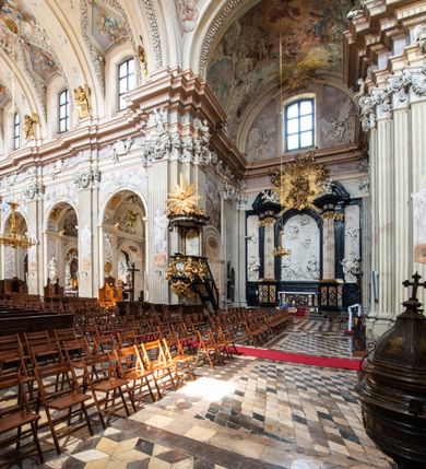 Zdjęcie nr 5: Kościół jest murowany z cegły, z użyciem ciosu kamiennego w partii cokołu i jako okładziny, tynkowany, z kryptami odpowiadającymi rzutowi. Założony jest na rzucie krzyża łacińskiego, z czteroprzęsłową nawą ujętą kaplicami, trójprzęsłowym prezbiterium zamknięty prosto, półtoraprzęsłowymi ramionami nawy poprzecznej, wysuniętymi poza korpus, zamknięte prosto i z kopułą na skrzyżowaniu naw. Przęsło fasady jest ujęte dwiema lokalnościami i dwiema wysuniętymi poza obręb korpusu wieżami z okrągłymi klatkami schodowymi z drewnianymi kręconymi schodami prowadzącymi do pomieszczeń nad lokalnościami. Do prezbiterium przylegają od południowego wschodu zakrystia, od północnego zachodu skarbiec, z składzikami na piętrze. 
Nawa jest artykułowa za pomocą pilastrów kompozytowych, zdwojonych w prezbiterium, transepcie i nawie głównej, zwielokrotniony w krzyżu kościoła, dźwigających wydatne belkowanie. Ściany kaplic są artykułowane za pomocą płytkich, opilastrowanych arkad; mury tarczowe kaplic wydzielone za pomocą gzymsu przełamującego się w narożnikach. Nawa i prezbiterium są sklepione kolebkami na gurtach z lunetami, transept sklepieniem kolebkowym na gurtach, kaplice pseudokopułami na pendentywach (w kaplicy Matki Boskiej i św. Katarzyny kopuły na rzucie elipsy z latarniami), zakrystia i skarbiec sklepieniem krzyżowo-kolebkowo, a przedsionki – nieckowym z lustrem. Okna nawy głównej i prezbiterium w profilowanych obramieniach, prostokątne, zamknięte łukiem segmentowym, okna kaplic są półkoliste. Bęben kopuły rozczłonkowany parami pilastrów kompozytowych, a między nimi rozlokowane naprzemian półkoliście zamknięte nisze i prostokątne okna. Do kościoła prowadzą drzwi wejściowe i para drzwi bocznych, z prezbiterium drzwi wejściowe do skarbca i zakrystii, z zakrystii na dziedziniec przy kościele. 
Fasada poprzedzona schodami, dwukondygnacyjna, dwuwieżowa, w dolnej kondygnacji siedmioosiowa, w górnej trójosiowa z dwiema wyodrębnionymi wieżami. Dolna kondygnacja rozczłonkowana zwojonymi pilastrami i parami kolumn flankujących oś środkową, o kapitelach kompozytowych, podtrzymujących wyłamujące się nad nimi belkowanie z wydatnym gzymsem i attyką, ponad belkowaniem w osi środkowej przerwany przyczółek. Górną kondygnację ujmują pary pilastrów ze stojącymi na ich tle wazonami, dźwigające wyłamujące się nad nimi belkowanie, w części środkowej zwieńczone przyczółkiem, w wieżach – miedzianymi hełmami. 
W części środkowej dolnej kondygnacji znajduje się zamknięta półkoliście wnęka z portalem, ujętym ukośnie dostawionymi pilastrami z konsolami podtrzymującymi naczółki i z tablicą z wklęsłymi bokami, zwieńczoną gzymsem w kształcie łuku nadwieszonego; ponad tablicą znajduje się półkoliste okno. Nad drzwiami bocznymi płaskorzeźbione postacie klęczących aniołów i kwadratowe okna, w wieżach wnęki z figurami św. Bernarda (po lewej) i św. Jana Kantego (po prawej). W części środkowej drugiej kondygnacji umieszczone jest prostokątne okno zamknięte łukiem segmentowym i zwieńczone przerwanym przyczółkiem. W polach bocznych nisze z figurami św. Kazimierza (po lewej) i św. Floriana (po prawej). Ściany boczne wzmocnione szkarpami, podzielone lizenami i pilastrami toskańskimi w dolnej kondygnacji prezbiterium oraz południowo wschodniej i północno zachodniej ścianie transeptu. Prezbiterium i ramiona transeptu zamknięte trójkątnymi szczytami z owalnymi oknami. Tambur kopuły rozczłonkowany lizenami, z oknami zamkniętymi łukami segmentowymi, w profilowanych obramieniach; ośmiopolową kopułę krytą blachą wieńczy latarnia opięta półkolumnami, pomiędzy którymi znajdują się wąskie okna zamknięte półkoliście. Nawę, prezbiterium i transept nakrywa dach siodłowy, nad pozostałymi pomieszczeniami dachy siodłowe, z wyjątkiem środkowych kaplic, w których kopułki wtopione zostały w dach i zwieńczone latarniami.  
