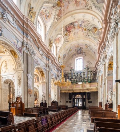 Zdjęcie nr 12: Kościół jest murowany z cegły, z użyciem ciosu kamiennego w partii cokołu i jako okładziny, tynkowany, z kryptami odpowiadającymi rzutowi. Założony jest na rzucie krzyża łacińskiego, z czteroprzęsłową nawą ujętą kaplicami, trójprzęsłowym prezbiterium zamknięty prosto, półtoraprzęsłowymi ramionami nawy poprzecznej, wysuniętymi poza korpus, zamknięte prosto i z kopułą na skrzyżowaniu naw. Przęsło fasady jest ujęte dwiema lokalnościami i dwiema wysuniętymi poza obręb korpusu wieżami z okrągłymi klatkami schodowymi z drewnianymi kręconymi schodami prowadzącymi do pomieszczeń nad lokalnościami. Do prezbiterium przylegają od południowego wschodu zakrystia, od północnego zachodu skarbiec, z składzikami na piętrze. 
Nawa jest artykułowa za pomocą pilastrów kompozytowych, zdwojonych w prezbiterium, transepcie i nawie głównej, zwielokrotniony w krzyżu kościoła, dźwigających wydatne belkowanie. Ściany kaplic są artykułowane za pomocą płytkich, opilastrowanych arkad; mury tarczowe kaplic wydzielone za pomocą gzymsu przełamującego się w narożnikach. Nawa i prezbiterium są sklepione kolebkami na gurtach z lunetami, transept sklepieniem kolebkowym na gurtach, kaplice pseudokopułami na pendentywach (w kaplicy Matki Boskiej i św. Katarzyny kopuły na rzucie elipsy z latarniami), zakrystia i skarbiec sklepieniem krzyżowo-kolebkowo, a przedsionki – nieckowym z lustrem. Okna nawy głównej i prezbiterium w profilowanych obramieniach, prostokątne, zamknięte łukiem segmentowym, okna kaplic są półkoliste. Bęben kopuły rozczłonkowany parami pilastrów kompozytowych, a między nimi rozlokowane naprzemian półkoliście zamknięte nisze i prostokątne okna. Do kościoła prowadzą drzwi wejściowe i para drzwi bocznych, z prezbiterium drzwi wejściowe do skarbca i zakrystii, z zakrystii na dziedziniec przy kościele. 
Fasada poprzedzona schodami, dwukondygnacyjna, dwuwieżowa, w dolnej kondygnacji siedmioosiowa, w górnej trójosiowa z dwiema wyodrębnionymi wieżami. Dolna kondygnacja rozczłonkowana zwojonymi pilastrami i parami kolumn flankujących oś środkową, o kapitelach kompozytowych, podtrzymujących wyłamujące się nad nimi belkowanie z wydatnym gzymsem i attyką, ponad belkowaniem w osi środkowej przerwany przyczółek. Górną kondygnację ujmują pary pilastrów ze stojącymi na ich tle wazonami, dźwigające wyłamujące się nad nimi belkowanie, w części środkowej zwieńczone przyczółkiem, w wieżach – miedzianymi hełmami. 
W części środkowej dolnej kondygnacji znajduje się zamknięta półkoliście wnęka z portalem, ujętym ukośnie dostawionymi pilastrami z konsolami podtrzymującymi naczółki i z tablicą z wklęsłymi bokami, zwieńczoną gzymsem w kształcie łuku nadwieszonego; ponad tablicą znajduje się półkoliste okno. Nad drzwiami bocznymi płaskorzeźbione postacie klęczących aniołów i kwadratowe okna, w wieżach wnęki z figurami św. Bernarda (po lewej) i św. Jana Kantego (po prawej). W części środkowej drugiej kondygnacji umieszczone jest prostokątne okno zamknięte łukiem segmentowym i zwieńczone przerwanym przyczółkiem. W polach bocznych nisze z figurami św. Kazimierza (po lewej) i św. Floriana (po prawej). Ściany boczne wzmocnione szkarpami, podzielone lizenami i pilastrami toskańskimi w dolnej kondygnacji prezbiterium oraz południowo wschodniej i północno zachodniej ścianie transeptu. Prezbiterium i ramiona transeptu zamknięte trójkątnymi szczytami z owalnymi oknami. Tambur kopuły rozczłonkowany lizenami, z oknami zamkniętymi łukami segmentowymi, w profilowanych obramieniach; ośmiopolową kopułę krytą blachą wieńczy latarnia opięta półkolumnami, pomiędzy którymi znajdują się wąskie okna zamknięte półkoliście. Nawę, prezbiterium i transept nakrywa dach siodłowy, nad pozostałymi pomieszczeniami dachy siodłowe, z wyjątkiem środkowych kaplic, w których kopułki wtopione zostały w dach i zwieńczone latarniami.  
