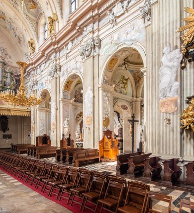 Zdjęcie nr 3: Kościół jest murowany z cegły, z użyciem ciosu kamiennego w partii cokołu i jako okładziny, tynkowany, z kryptami odpowiadającymi rzutowi. Założony jest na rzucie krzyża łacińskiego, z czteroprzęsłową nawą ujętą kaplicami, trójprzęsłowym prezbiterium zamknięty prosto, półtoraprzęsłowymi ramionami nawy poprzecznej, wysuniętymi poza korpus, zamknięte prosto i z kopułą na skrzyżowaniu naw. Przęsło fasady jest ujęte dwiema lokalnościami i dwiema wysuniętymi poza obręb korpusu wieżami z okrągłymi klatkami schodowymi z drewnianymi kręconymi schodami prowadzącymi do pomieszczeń nad lokalnościami. Do prezbiterium przylegają od południowego wschodu zakrystia, od północnego zachodu skarbiec, z składzikami na piętrze. 
Nawa jest artykułowa za pomocą pilastrów kompozytowych, zdwojonych w prezbiterium, transepcie i nawie głównej, zwielokrotniony w krzyżu kościoła, dźwigających wydatne belkowanie. Ściany kaplic są artykułowane za pomocą płytkich, opilastrowanych arkad; mury tarczowe kaplic wydzielone za pomocą gzymsu przełamującego się w narożnikach. Nawa i prezbiterium są sklepione kolebkami na gurtach z lunetami, transept sklepieniem kolebkowym na gurtach, kaplice pseudokopułami na pendentywach (w kaplicy Matki Boskiej i św. Katarzyny kopuły na rzucie elipsy z latarniami), zakrystia i skarbiec sklepieniem krzyżowo-kolebkowo, a przedsionki – nieckowym z lustrem. Okna nawy głównej i prezbiterium w profilowanych obramieniach, prostokątne, zamknięte łukiem segmentowym, okna kaplic są półkoliste. Bęben kopuły rozczłonkowany parami pilastrów kompozytowych, a między nimi rozlokowane naprzemian półkoliście zamknięte nisze i prostokątne okna. Do kościoła prowadzą drzwi wejściowe i para drzwi bocznych, z prezbiterium drzwi wejściowe do skarbca i zakrystii, z zakrystii na dziedziniec przy kościele. 
Fasada poprzedzona schodami, dwukondygnacyjna, dwuwieżowa, w dolnej kondygnacji siedmioosiowa, w górnej trójosiowa z dwiema wyodrębnionymi wieżami. Dolna kondygnacja rozczłonkowana zwojonymi pilastrami i parami kolumn flankujących oś środkową, o kapitelach kompozytowych, podtrzymujących wyłamujące się nad nimi belkowanie z wydatnym gzymsem i attyką, ponad belkowaniem w osi środkowej przerwany przyczółek. Górną kondygnację ujmują pary pilastrów ze stojącymi na ich tle wazonami, dźwigające wyłamujące się nad nimi belkowanie, w części środkowej zwieńczone przyczółkiem, w wieżach – miedzianymi hełmami. 
W części środkowej dolnej kondygnacji znajduje się zamknięta półkoliście wnęka z portalem, ujętym ukośnie dostawionymi pilastrami z konsolami podtrzymującymi naczółki i z tablicą z wklęsłymi bokami, zwieńczoną gzymsem w kształcie łuku nadwieszonego; ponad tablicą znajduje się półkoliste okno. Nad drzwiami bocznymi płaskorzeźbione postacie klęczących aniołów i kwadratowe okna, w wieżach wnęki z figurami św. Bernarda (po lewej) i św. Jana Kantego (po prawej). W części środkowej drugiej kondygnacji umieszczone jest prostokątne okno zamknięte łukiem segmentowym i zwieńczone przerwanym przyczółkiem. W polach bocznych nisze z figurami św. Kazimierza (po lewej) i św. Floriana (po prawej). Ściany boczne wzmocnione szkarpami, podzielone lizenami i pilastrami toskańskimi w dolnej kondygnacji prezbiterium oraz południowo wschodniej i północno zachodniej ścianie transeptu. Prezbiterium i ramiona transeptu zamknięte trójkątnymi szczytami z owalnymi oknami. Tambur kopuły rozczłonkowany lizenami, z oknami zamkniętymi łukami segmentowymi, w profilowanych obramieniach; ośmiopolową kopułę krytą blachą wieńczy latarnia opięta półkolumnami, pomiędzy którymi znajdują się wąskie okna zamknięte półkoliście. Nawę, prezbiterium i transept nakrywa dach siodłowy, nad pozostałymi pomieszczeniami dachy siodłowe, z wyjątkiem środkowych kaplic, w których kopułki wtopione zostały w dach i zwieńczone latarniami.  
