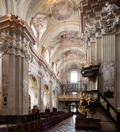 Zdjęcie nr 10: Kościół jest murowany z cegły, z użyciem ciosu kamiennego w partii cokołu i jako okładziny, tynkowany, z kryptami odpowiadającymi rzutowi. Założony jest na rzucie krzyża łacińskiego, z czteroprzęsłową nawą ujętą kaplicami, trójprzęsłowym prezbiterium zamknięty prosto, półtoraprzęsłowymi ramionami nawy poprzecznej, wysuniętymi poza korpus, zamknięte prosto i z kopułą na skrzyżowaniu naw. Przęsło fasady jest ujęte dwiema lokalnościami i dwiema wysuniętymi poza obręb korpusu wieżami z okrągłymi klatkami schodowymi z drewnianymi kręconymi schodami prowadzącymi do pomieszczeń nad lokalnościami. Do prezbiterium przylegają od południowego wschodu zakrystia, od północnego zachodu skarbiec, z składzikami na piętrze. 
Nawa jest artykułowa za pomocą pilastrów kompozytowych, zdwojonych w prezbiterium, transepcie i nawie głównej, zwielokrotniony w krzyżu kościoła, dźwigających wydatne belkowanie. Ściany kaplic są artykułowane za pomocą płytkich, opilastrowanych arkad; mury tarczowe kaplic wydzielone za pomocą gzymsu przełamującego się w narożnikach. Nawa i prezbiterium są sklepione kolebkami na gurtach z lunetami, transept sklepieniem kolebkowym na gurtach, kaplice pseudokopułami na pendentywach (w kaplicy Matki Boskiej i św. Katarzyny kopuły na rzucie elipsy z latarniami), zakrystia i skarbiec sklepieniem krzyżowo-kolebkowo, a przedsionki – nieckowym z lustrem. Okna nawy głównej i prezbiterium w profilowanych obramieniach, prostokątne, zamknięte łukiem segmentowym, okna kaplic są półkoliste. Bęben kopuły rozczłonkowany parami pilastrów kompozytowych, a między nimi rozlokowane naprzemian półkoliście zamknięte nisze i prostokątne okna. Do kościoła prowadzą drzwi wejściowe i para drzwi bocznych, z prezbiterium drzwi wejściowe do skarbca i zakrystii, z zakrystii na dziedziniec przy kościele. 
Fasada poprzedzona schodami, dwukondygnacyjna, dwuwieżowa, w dolnej kondygnacji siedmioosiowa, w górnej trójosiowa z dwiema wyodrębnionymi wieżami. Dolna kondygnacja rozczłonkowana zwojonymi pilastrami i parami kolumn flankujących oś środkową, o kapitelach kompozytowych, podtrzymujących wyłamujące się nad nimi belkowanie z wydatnym gzymsem i attyką, ponad belkowaniem w osi środkowej przerwany przyczółek. Górną kondygnację ujmują pary pilastrów ze stojącymi na ich tle wazonami, dźwigające wyłamujące się nad nimi belkowanie, w części środkowej zwieńczone przyczółkiem, w wieżach – miedzianymi hełmami. 
W części środkowej dolnej kondygnacji znajduje się zamknięta półkoliście wnęka z portalem, ujętym ukośnie dostawionymi pilastrami z konsolami podtrzymującymi naczółki i z tablicą z wklęsłymi bokami, zwieńczoną gzymsem w kształcie łuku nadwieszonego; ponad tablicą znajduje się półkoliste okno. Nad drzwiami bocznymi płaskorzeźbione postacie klęczących aniołów i kwadratowe okna, w wieżach wnęki z figurami św. Bernarda (po lewej) i św. Jana Kantego (po prawej). W części środkowej drugiej kondygnacji umieszczone jest prostokątne okno zamknięte łukiem segmentowym i zwieńczone przerwanym przyczółkiem. W polach bocznych nisze z figurami św. Kazimierza (po lewej) i św. Floriana (po prawej). Ściany boczne wzmocnione szkarpami, podzielone lizenami i pilastrami toskańskimi w dolnej kondygnacji prezbiterium oraz południowo wschodniej i północno zachodniej ścianie transeptu. Prezbiterium i ramiona transeptu zamknięte trójkątnymi szczytami z owalnymi oknami. Tambur kopuły rozczłonkowany lizenami, z oknami zamkniętymi łukami segmentowymi, w profilowanych obramieniach; ośmiopolową kopułę krytą blachą wieńczy latarnia opięta półkolumnami, pomiędzy którymi znajdują się wąskie okna zamknięte półkoliście. Nawę, prezbiterium i transept nakrywa dach siodłowy, nad pozostałymi pomieszczeniami dachy siodłowe, z wyjątkiem środkowych kaplic, w których kopułki wtopione zostały w dach i zwieńczone latarniami.  
