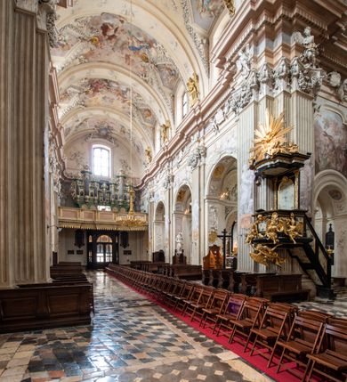 Zdjęcie nr 16: Kościół jest murowany z cegły, z użyciem ciosu kamiennego w partii cokołu i jako okładziny, tynkowany, z kryptami odpowiadającymi rzutowi. Założony jest na rzucie krzyża łacińskiego, z czteroprzęsłową nawą ujętą kaplicami, trójprzęsłowym prezbiterium zamknięty prosto, półtoraprzęsłowymi ramionami nawy poprzecznej, wysuniętymi poza korpus, zamknięte prosto i z kopułą na skrzyżowaniu naw. Przęsło fasady jest ujęte dwiema lokalnościami i dwiema wysuniętymi poza obręb korpusu wieżami z okrągłymi klatkami schodowymi z drewnianymi kręconymi schodami prowadzącymi do pomieszczeń nad lokalnościami. Do prezbiterium przylegają od południowego wschodu zakrystia, od północnego zachodu skarbiec, z składzikami na piętrze. 
Nawa jest artykułowa za pomocą pilastrów kompozytowych, zdwojonych w prezbiterium, transepcie i nawie głównej, zwielokrotniony w krzyżu kościoła, dźwigających wydatne belkowanie. Ściany kaplic są artykułowane za pomocą płytkich, opilastrowanych arkad; mury tarczowe kaplic wydzielone za pomocą gzymsu przełamującego się w narożnikach. Nawa i prezbiterium są sklepione kolebkami na gurtach z lunetami, transept sklepieniem kolebkowym na gurtach, kaplice pseudokopułami na pendentywach (w kaplicy Matki Boskiej i św. Katarzyny kopuły na rzucie elipsy z latarniami), zakrystia i skarbiec sklepieniem krzyżowo-kolebkowo, a przedsionki – nieckowym z lustrem. Okna nawy głównej i prezbiterium w profilowanych obramieniach, prostokątne, zamknięte łukiem segmentowym, okna kaplic są półkoliste. Bęben kopuły rozczłonkowany parami pilastrów kompozytowych, a między nimi rozlokowane naprzemian półkoliście zamknięte nisze i prostokątne okna. Do kościoła prowadzą drzwi wejściowe i para drzwi bocznych, z prezbiterium drzwi wejściowe do skarbca i zakrystii, z zakrystii na dziedziniec przy kościele. 
Fasada poprzedzona schodami, dwukondygnacyjna, dwuwieżowa, w dolnej kondygnacji siedmioosiowa, w górnej trójosiowa z dwiema wyodrębnionymi wieżami. Dolna kondygnacja rozczłonkowana zwojonymi pilastrami i parami kolumn flankujących oś środkową, o kapitelach kompozytowych, podtrzymujących wyłamujące się nad nimi belkowanie z wydatnym gzymsem i attyką, ponad belkowaniem w osi środkowej przerwany przyczółek. Górną kondygnację ujmują pary pilastrów ze stojącymi na ich tle wazonami, dźwigające wyłamujące się nad nimi belkowanie, w części środkowej zwieńczone przyczółkiem, w wieżach – miedzianymi hełmami. 
W części środkowej dolnej kondygnacji znajduje się zamknięta półkoliście wnęka z portalem, ujętym ukośnie dostawionymi pilastrami z konsolami podtrzymującymi naczółki i z tablicą z wklęsłymi bokami, zwieńczoną gzymsem w kształcie łuku nadwieszonego; ponad tablicą znajduje się półkoliste okno. Nad drzwiami bocznymi płaskorzeźbione postacie klęczących aniołów i kwadratowe okna, w wieżach wnęki z figurami św. Bernarda (po lewej) i św. Jana Kantego (po prawej). W części środkowej drugiej kondygnacji umieszczone jest prostokątne okno zamknięte łukiem segmentowym i zwieńczone przerwanym przyczółkiem. W polach bocznych nisze z figurami św. Kazimierza (po lewej) i św. Floriana (po prawej). Ściany boczne wzmocnione szkarpami, podzielone lizenami i pilastrami toskańskimi w dolnej kondygnacji prezbiterium oraz południowo wschodniej i północno zachodniej ścianie transeptu. Prezbiterium i ramiona transeptu zamknięte trójkątnymi szczytami z owalnymi oknami. Tambur kopuły rozczłonkowany lizenami, z oknami zamkniętymi łukami segmentowymi, w profilowanych obramieniach; ośmiopolową kopułę krytą blachą wieńczy latarnia opięta półkolumnami, pomiędzy którymi znajdują się wąskie okna zamknięte półkoliście. Nawę, prezbiterium i transept nakrywa dach siodłowy, nad pozostałymi pomieszczeniami dachy siodłowe, z wyjątkiem środkowych kaplic, w których kopułki wtopione zostały w dach i zwieńczone latarniami.  
