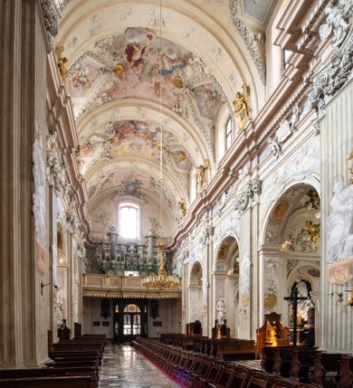 Zdjęcie nr 11: Kościół jest murowany z cegły, z użyciem ciosu kamiennego w partii cokołu i jako okładziny, tynkowany, z kryptami odpowiadającymi rzutowi. Założony jest na rzucie krzyża łacińskiego, z czteroprzęsłową nawą ujętą kaplicami, trójprzęsłowym prezbiterium zamknięty prosto, półtoraprzęsłowymi ramionami nawy poprzecznej, wysuniętymi poza korpus, zamknięte prosto i z kopułą na skrzyżowaniu naw. Przęsło fasady jest ujęte dwiema lokalnościami i dwiema wysuniętymi poza obręb korpusu wieżami z okrągłymi klatkami schodowymi z drewnianymi kręconymi schodami prowadzącymi do pomieszczeń nad lokalnościami. Do prezbiterium przylegają od południowego wschodu zakrystia, od północnego zachodu skarbiec, z składzikami na piętrze. 
Nawa jest artykułowa za pomocą pilastrów kompozytowych, zdwojonych w prezbiterium, transepcie i nawie głównej, zwielokrotniony w krzyżu kościoła, dźwigających wydatne belkowanie. Ściany kaplic są artykułowane za pomocą płytkich, opilastrowanych arkad; mury tarczowe kaplic wydzielone za pomocą gzymsu przełamującego się w narożnikach. Nawa i prezbiterium są sklepione kolebkami na gurtach z lunetami, transept sklepieniem kolebkowym na gurtach, kaplice pseudokopułami na pendentywach (w kaplicy Matki Boskiej i św. Katarzyny kopuły na rzucie elipsy z latarniami), zakrystia i skarbiec sklepieniem krzyżowo-kolebkowo, a przedsionki – nieckowym z lustrem. Okna nawy głównej i prezbiterium w profilowanych obramieniach, prostokątne, zamknięte łukiem segmentowym, okna kaplic są półkoliste. Bęben kopuły rozczłonkowany parami pilastrów kompozytowych, a między nimi rozlokowane naprzemian półkoliście zamknięte nisze i prostokątne okna. Do kościoła prowadzą drzwi wejściowe i para drzwi bocznych, z prezbiterium drzwi wejściowe do skarbca i zakrystii, z zakrystii na dziedziniec przy kościele. 
Fasada poprzedzona schodami, dwukondygnacyjna, dwuwieżowa, w dolnej kondygnacji siedmioosiowa, w górnej trójosiowa z dwiema wyodrębnionymi wieżami. Dolna kondygnacja rozczłonkowana zwojonymi pilastrami i parami kolumn flankujących oś środkową, o kapitelach kompozytowych, podtrzymujących wyłamujące się nad nimi belkowanie z wydatnym gzymsem i attyką, ponad belkowaniem w osi środkowej przerwany przyczółek. Górną kondygnację ujmują pary pilastrów ze stojącymi na ich tle wazonami, dźwigające wyłamujące się nad nimi belkowanie, w części środkowej zwieńczone przyczółkiem, w wieżach – miedzianymi hełmami. 
W części środkowej dolnej kondygnacji znajduje się zamknięta półkoliście wnęka z portalem, ujętym ukośnie dostawionymi pilastrami z konsolami podtrzymującymi naczółki i z tablicą z wklęsłymi bokami, zwieńczoną gzymsem w kształcie łuku nadwieszonego; ponad tablicą znajduje się półkoliste okno. Nad drzwiami bocznymi płaskorzeźbione postacie klęczących aniołów i kwadratowe okna, w wieżach wnęki z figurami św. Bernarda (po lewej) i św. Jana Kantego (po prawej). W części środkowej drugiej kondygnacji umieszczone jest prostokątne okno zamknięte łukiem segmentowym i zwieńczone przerwanym przyczółkiem. W polach bocznych nisze z figurami św. Kazimierza (po lewej) i św. Floriana (po prawej). Ściany boczne wzmocnione szkarpami, podzielone lizenami i pilastrami toskańskimi w dolnej kondygnacji prezbiterium oraz południowo wschodniej i północno zachodniej ścianie transeptu. Prezbiterium i ramiona transeptu zamknięte trójkątnymi szczytami z owalnymi oknami. Tambur kopuły rozczłonkowany lizenami, z oknami zamkniętymi łukami segmentowymi, w profilowanych obramieniach; ośmiopolową kopułę krytą blachą wieńczy latarnia opięta półkolumnami, pomiędzy którymi znajdują się wąskie okna zamknięte półkoliście. Nawę, prezbiterium i transept nakrywa dach siodłowy, nad pozostałymi pomieszczeniami dachy siodłowe, z wyjątkiem środkowych kaplic, w których kopułki wtopione zostały w dach i zwieńczone latarniami.  
