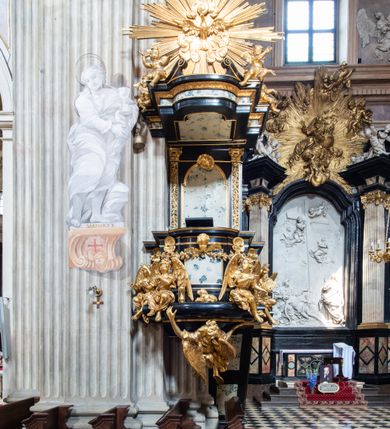 Zdjęcie nr 21: Kościół jest murowany z cegły, z użyciem ciosu kamiennego w partii cokołu i jako okładziny, tynkowany, z kryptami odpowiadającymi rzutowi. Założony jest na rzucie krzyża łacińskiego, z czteroprzęsłową nawą ujętą kaplicami, trójprzęsłowym prezbiterium zamknięty prosto, półtoraprzęsłowymi ramionami nawy poprzecznej, wysuniętymi poza korpus, zamknięte prosto i z kopułą na skrzyżowaniu naw. Przęsło fasady jest ujęte dwiema lokalnościami i dwiema wysuniętymi poza obręb korpusu wieżami z okrągłymi klatkami schodowymi z drewnianymi kręconymi schodami prowadzącymi do pomieszczeń nad lokalnościami. Do prezbiterium przylegają od południowego wschodu zakrystia, od północnego zachodu skarbiec, z składzikami na piętrze. 
Nawa jest artykułowa za pomocą pilastrów kompozytowych, zdwojonych w prezbiterium, transepcie i nawie głównej, zwielokrotniony w krzyżu kościoła, dźwigających wydatne belkowanie. Ściany kaplic są artykułowane za pomocą płytkich, opilastrowanych arkad; mury tarczowe kaplic wydzielone za pomocą gzymsu przełamującego się w narożnikach. Nawa i prezbiterium są sklepione kolebkami na gurtach z lunetami, transept sklepieniem kolebkowym na gurtach, kaplice pseudokopułami na pendentywach (w kaplicy Matki Boskiej i św. Katarzyny kopuły na rzucie elipsy z latarniami), zakrystia i skarbiec sklepieniem krzyżowo-kolebkowo, a przedsionki – nieckowym z lustrem. Okna nawy głównej i prezbiterium w profilowanych obramieniach, prostokątne, zamknięte łukiem segmentowym, okna kaplic są półkoliste. Bęben kopuły rozczłonkowany parami pilastrów kompozytowych, a między nimi rozlokowane naprzemian półkoliście zamknięte nisze i prostokątne okna. Do kościoła prowadzą drzwi wejściowe i para drzwi bocznych, z prezbiterium drzwi wejściowe do skarbca i zakrystii, z zakrystii na dziedziniec przy kościele. 
Fasada poprzedzona schodami, dwukondygnacyjna, dwuwieżowa, w dolnej kondygnacji siedmioosiowa, w górnej trójosiowa z dwiema wyodrębnionymi wieżami. Dolna kondygnacja rozczłonkowana zwojonymi pilastrami i parami kolumn flankujących oś środkową, o kapitelach kompozytowych, podtrzymujących wyłamujące się nad nimi belkowanie z wydatnym gzymsem i attyką, ponad belkowaniem w osi środkowej przerwany przyczółek. Górną kondygnację ujmują pary pilastrów ze stojącymi na ich tle wazonami, dźwigające wyłamujące się nad nimi belkowanie, w części środkowej zwieńczone przyczółkiem, w wieżach – miedzianymi hełmami. 
W części środkowej dolnej kondygnacji znajduje się zamknięta półkoliście wnęka z portalem, ujętym ukośnie dostawionymi pilastrami z konsolami podtrzymującymi naczółki i z tablicą z wklęsłymi bokami, zwieńczoną gzymsem w kształcie łuku nadwieszonego; ponad tablicą znajduje się półkoliste okno. Nad drzwiami bocznymi płaskorzeźbione postacie klęczących aniołów i kwadratowe okna, w wieżach wnęki z figurami św. Bernarda (po lewej) i św. Jana Kantego (po prawej). W części środkowej drugiej kondygnacji umieszczone jest prostokątne okno zamknięte łukiem segmentowym i zwieńczone przerwanym przyczółkiem. W polach bocznych nisze z figurami św. Kazimierza (po lewej) i św. Floriana (po prawej). Ściany boczne wzmocnione szkarpami, podzielone lizenami i pilastrami toskańskimi w dolnej kondygnacji prezbiterium oraz południowo wschodniej i północno zachodniej ścianie transeptu. Prezbiterium i ramiona transeptu zamknięte trójkątnymi szczytami z owalnymi oknami. Tambur kopuły rozczłonkowany lizenami, z oknami zamkniętymi łukami segmentowymi, w profilowanych obramieniach; ośmiopolową kopułę krytą blachą wieńczy latarnia opięta półkolumnami, pomiędzy którymi znajdują się wąskie okna zamknięte półkoliście. Nawę, prezbiterium i transept nakrywa dach siodłowy, nad pozostałymi pomieszczeniami dachy siodłowe, z wyjątkiem środkowych kaplic, w których kopułki wtopione zostały w dach i zwieńczone latarniami.  
