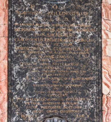 Zdjęcie nr 4: Epitafium w kształcie pionowej płyty, ujętej spływami wolutowymi z kampanulami, z owalnym polem na portret, zwieńczonym profilowanym, falistym gzymsem. U dołu kartusz z herbem własnym (róża przebita strzałą) pod kapeluszem kanonickim, zwieńczony muszlą. Portret ujęty profilowaniem z dwiema zawiniętym na zewnątrz taśmami, przedstawia mężczyznę w popiersiu, w czerwonej pelerynie z zielonymi befkami, z orłem na łańcuchu, z głową ukazaną w trzech czwartych, zwróconą lekko w prawą stronę. Jego twarz jest pełna, o zaczerwienionych policzkach, nos szeroki, oczy otwarte w płytkich oczodołach, spoglądają wprost, usta zamknięte, lekko uśmiechnięte, wyraziście zaznaczone czerwienią. Włosy jasne, zaczesane do tyłu, sięgające szyi, sprawiające wrażenie peruki. Tło nieokreślone, ciemne, w tonacji szarej. Tablica z inskrypcją prostokątna, o zaoblonych, ujętych ceownicami narożach i wyciętych niemal półkoliście krótszych bokach, w niej złocona inskrypcja: "D(EO) O(PTIMO) M(AXIMO) / M. ANTONIUS. ZOŁĘDZIOWSKI / U(TRIUSQUE) J(URIS) S(AGRE) T(HEOLOGIAE) D(OCTOR) P(ROFESSORI) / IN. ACADEMIA. ARCADUM. NORINDUS. CALCEDONIUS. / RECTOR. UNIVERSITATIS. SEPTENNIO. MAGNIFICUS. /  PROCANCELLARUS. / CRACOVIENSIS. CATHEDRALIS. CANONICUS. / APUD. S(UMMI) P(ONTIFICES) MM. / BENEDICTUM. XIV. CLEMENTEM. XIII. / PRO. REFERENDO. III. ALBUM. SANCTORUM. / DIVO. IOANNE. CANTIO. / TRIBUS. LUSTRIS. / FELIX. IN. URBE. POSTULATOR. / PIUS. IUSTUS. LIBERALIS. CARUS. / CUM. VIXISSET. TERRIS. ANNOS. LXXII. / ASTRA. PETIIT. / AE. C. MDCCLXXXIII. IX. KAL(ENDAS) SEPTEMBRIS. / HIC. / RESURRECTIONEM. MORTUORUM. / ET. / VITAM. VENTURI. SECULI. / EXPECTAT. / M(AGNAE) M(AGISTRI) IOSEPHUS. ALOYSIUS. PUTANOWICZ. / PETRUS. IOSEPHUS. RYDULSKI. / SACREA. THEOLOGIE. DOCTORES. / MAESTI. GRATI. EXEQVUTORES. / POSUERE". 