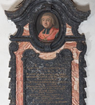 Zdjęcie nr 1: Epitafium w kształcie pionowej płyty, ujętej spływami wolutowymi z kampanulami, z owalnym polem na portret, zwieńczonym profilowanym, falistym gzymsem. U dołu kartusz z herbem własnym (róża przebita strzałą) pod kapeluszem kanonickim, zwieńczony muszlą. Portret ujęty profilowaniem z dwiema zawiniętym na zewnątrz taśmami, przedstawia mężczyznę w popiersiu, w czerwonej pelerynie z zielonymi befkami, z orłem na łańcuchu, z głową ukazaną w trzech czwartych, zwróconą lekko w prawą stronę. Jego twarz jest pełna, o zaczerwienionych policzkach, nos szeroki, oczy otwarte w płytkich oczodołach, spoglądają wprost, usta zamknięte, lekko uśmiechnięte, wyraziście zaznaczone czerwienią. Włosy jasne, zaczesane do tyłu, sięgające szyi, sprawiające wrażenie peruki. Tło nieokreślone, ciemne, w tonacji szarej. Tablica z inskrypcją prostokątna, o zaoblonych, ujętych ceownicami narożach i wyciętych niemal półkoliście krótszych bokach, w niej złocona inskrypcja: "D(EO) O(PTIMO) M(AXIMO) / M. ANTONIUS. ZOŁĘDZIOWSKI / U(TRIUSQUE) J(URIS) S(AGRE) T(HEOLOGIAE) D(OCTOR) P(ROFESSORI) / IN. ACADEMIA. ARCADUM. NORINDUS. CALCEDONIUS. / RECTOR. UNIVERSITATIS. SEPTENNIO. MAGNIFICUS. /  PROCANCELLARUS. / CRACOVIENSIS. CATHEDRALIS. CANONICUS. / APUD. S(UMMI) P(ONTIFICES) MM. / BENEDICTUM. XIV. CLEMENTEM. XIII. / PRO. REFERENDO. III. ALBUM. SANCTORUM. / DIVO. IOANNE. CANTIO. / TRIBUS. LUSTRIS. / FELIX. IN. URBE. POSTULATOR. / PIUS. IUSTUS. LIBERALIS. CARUS. / CUM. VIXISSET. TERRIS. ANNOS. LXXII. / ASTRA. PETIIT. / AE. C. MDCCLXXXIII. IX. KAL(ENDAS) SEPTEMBRIS. / HIC. / RESURRECTIONEM. MORTUORUM. / ET. / VITAM. VENTURI. SECULI. / EXPECTAT. / M(AGNAE) M(AGISTRI) IOSEPHUS. ALOYSIUS. PUTANOWICZ. / PETRUS. IOSEPHUS. RYDULSKI. / SACREA. THEOLOGIE. DOCTORES. / MAESTI. GRATI. EXEQVUTORES. / POSUERE". 