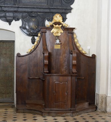 Zdjęcie nr 2: Para konfesjonałów o lekko wybrzuszonym przodzie i wklęsłych bokach, z wysokim zapleckiem ze ściętymi, wklęsłymi bokami, ujętymi spływami wolutowymi. Siedzisko z drzwiczkami ozdobionymi wklęsłą ramą z łukowatymi wcięciami na każdym boku i bokami wyciętymi linią wklęsło-wypukłą, z kratkami. Środkowa część zaplecka zwieńczona profilowanym gzymsem z łukiem nadwieszonymi, w którym znajduje się złocony kartusz ujęty karbowaną taśmą i muszlą palmetową z inskrypcją „KTÓRYCH ODPUŚCICIE / GRZECHY / SĄ IM ODPUSZCZONE / JAN XX. 23”. Nad łukiem muszla palmetowa ujęta wiciami akantu. Wzdłuż spływów wolutowych po bokach złocone kampanule. Do zaplecka, nad siedziskiem zamontowana lampka elektryczna i tabliczka z inskrypcją „W TYM KONFESJONALE SPOWIADAŁ / bł(ogosławiony) Jan Paweł II / ks(iądz) Kardynał Karol Wojtyła / gdy był Pasterzem Kościoła Krakowskiego.”
