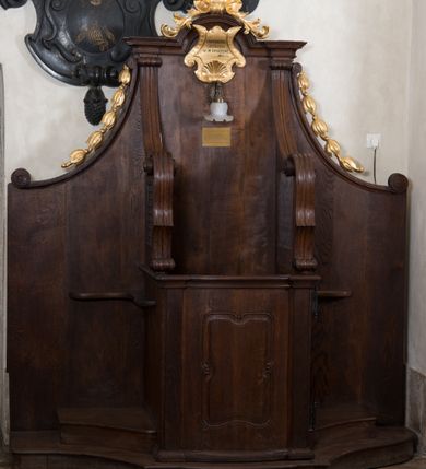 Zdjęcie nr 6: Para konfesjonałów o lekko wybrzuszonym przodzie i wklęsłych bokach, z wysokim zapleckiem ze ściętymi, wklęsłymi bokami, ujętymi spływami wolutowymi. Siedzisko z drzwiczkami ozdobionymi wklęsłą ramą z łukowatymi wcięciami na każdym boku i bokami wyciętymi linią wklęsło-wypukłą, z kratkami. Środkowa część zaplecka zwieńczona profilowanym gzymsem z łukiem nadwieszonymi, w którym znajduje się złocony kartusz ujęty karbowaną taśmą i muszlą palmetową z inskrypcją „KTÓRYCH ODPUŚCICIE / GRZECHY / SĄ IM ODPUSZCZONE / JAN XX. 23”. Nad łukiem muszla palmetowa ujęta wiciami akantu. Wzdłuż spływów wolutowych po bokach złocone kampanule. Do zaplecka, nad siedziskiem zamontowana lampka elektryczna i tabliczka z inskrypcją „W TYM KONFESJONALE SPOWIADAŁ / bł(ogosławiony) Jan Paweł II / ks(iądz) Kardynał Karol Wojtyła / gdy był Pasterzem Kościoła Krakowskiego.”
