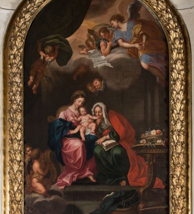 Zdjęcie nr 2: Obraz w kształcie stojącego prostokąta zamkniętego łukiem półkolistym, w złoconej ramie, ozdobionej wieńcem laurowym. W centrum kompozycji ukazana siedząca na fotelu Maria z Jezusem na kolanach i siedząca obok św. Anną w towarzystwie aniołów klęczących u ich stóp lub unoszących się w obłokach. Maria przedstawiona niemal frontalnie, przytrzymuje obiema rękami Jezusa siedzącego na jej lewym kolanie i pochyla głową lekko w lewo. Ubrana jest w różową, rozłożystą suknię i ciemnoniebieski płaszcz oraz brązową chustę na głowie. Jej twarz jest owalna, rysy łagodne, policzki lekko zaróżowione. Nos ma wąski i długi, oczy migdałowate, lekko przymknięte, usta wąskie, pełne, zaznaczone czerwienią. Widoczne spod chusty włosy są proste, opadają na plecy. Jezus siedzi frontalnie, z rozłożonymi nóżkami i rączkami, z których lewą trzyma i całuje św. Anna. Jego twarz jest pełna, policzki lekko zaokrąglone, nos krótki, oczy otwarte, a usta lekko rozwarte i uśmiechnięte, włosy na głowie krótkie, z kręconymi nieznacznie puklami. Dolną część podbrzusza i biodra okrywa biała pielucha. Anna jest ukazana niemal frontalnie, lekko pochylona w kierunku Marii i Jezusa, ubrana w zieloną suknię, czerwony płaszcz i białą chustę okrywającą głowę i szyję. Twarz wykazuje cechy starszej kobiety, z wyraźnymi zmarszczkami, z wyrazistym nosem, zamkniętymi oczami oraz ustami całującymi dłoń Jezusa. Na kolanach trzyma otwartą księgę. Po lewej stronie przy tronie klęczą na chmurach dwa nagie putta, o korpulentnych ciałach, kręconych włosach, z których jedno, na pierwszym planie jest zwrócone w kierunku głównych bohaterów, a drugie z tyłu patrzy na widza. W górnej części kompozycji, na obłoku unoszą się aniołowie, z których jeden, w prawej części kompozycji jest ukazany w całej postaci, w niebieskiej tunice i brązowym płaszczu, z rękami opuszczonymi ku dołowi i złożonymi w geście modlitwy, a głową ujętą z lewego profilu. Środkowy wychyla się zza chmury, okolony zieloną szatą, z lewą ręką złożoną na piersi. Trzeci anioł-putto trzyma pofalowaną kartkę z napisem: „GENERATIONEM EIUS QUIS ENARRABIT”. Po lewej stronie ukazany jest anioł podtrzymujący zieloną kotarę. Pod chmurą, tuż nad głową św. Anny, para uskrzydlonych główek anielskich. W prawej części kompozycji stolik na wolutowych nogach wspartych na lwich łapach i ozdobionych maszkaronami z koszem pełnym owoców oraz leżący na posadzce kosz wiklinowy z niewielką skrzynią i granatową tkaniną z białą podszewką.     

