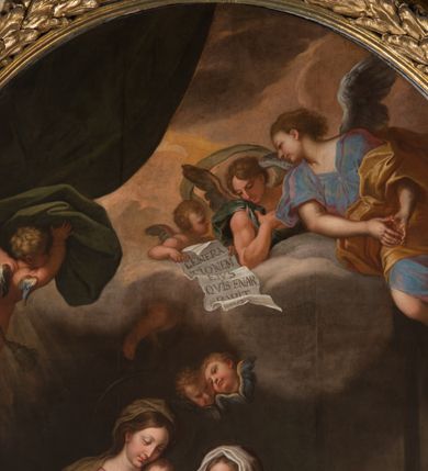 Zdjęcie nr 36: Obraz w kształcie stojącego prostokąta zamkniętego łukiem półkolistym, w złoconej ramie, ozdobionej wieńcem laurowym. W centrum kompozycji ukazana siedząca na fotelu Maria z Jezusem na kolanach i siedząca obok św. Anną w towarzystwie aniołów klęczących u ich stóp lub unoszących się w obłokach. Maria przedstawiona niemal frontalnie, przytrzymuje obiema rękami Jezusa siedzącego na jej lewym kolanie i pochyla głową lekko w lewo. Ubrana jest w różową, rozłożystą suknię i ciemnoniebieski płaszcz oraz brązową chustę na głowie. Jej twarz jest owalna, rysy łagodne, policzki lekko zaróżowione. Nos ma wąski i długi, oczy migdałowate, lekko przymknięte, usta wąskie, pełne, zaznaczone czerwienią. Widoczne spod chusty włosy są proste, opadają na plecy. Jezus siedzi frontalnie, z rozłożonymi nóżkami i rączkami, z których lewą trzyma i całuje św. Anna. Jego twarz jest pełna, policzki lekko zaokrąglone, nos krótki, oczy otwarte, a usta lekko rozwarte i uśmiechnięte, włosy na głowie krótkie, z kręconymi nieznacznie puklami. Dolną część podbrzusza i biodra okrywa biała pielucha. Anna jest ukazana niemal frontalnie, lekko pochylona w kierunku Marii i Jezusa, ubrana w zieloną suknię, czerwony płaszcz i białą chustę okrywającą głowę i szyję. Twarz wykazuje cechy starszej kobiety, z wyraźnymi zmarszczkami, z wyrazistym nosem, zamkniętymi oczami oraz ustami całującymi dłoń Jezusa. Na kolanach trzyma otwartą księgę. Po lewej stronie przy tronie klęczą na chmurach dwa nagie putta, o korpulentnych ciałach, kręconych włosach, z których jedno, na pierwszym planie jest zwrócone w kierunku głównych bohaterów, a drugie z tyłu patrzy na widza. W górnej części kompozycji, na obłoku unoszą się aniołowie, z których jeden, w prawej części kompozycji jest ukazany w całej postaci, w niebieskiej tunice i brązowym płaszczu, z rękami opuszczonymi ku dołowi i złożonymi w geście modlitwy, a głową ujętą z lewego profilu. Środkowy wychyla się zza chmury, okolony zieloną szatą, z lewą ręką złożoną na piersi. Trzeci anioł-putto trzyma pofalowaną kartkę z napisem: „GENERATIONEM EIUS QUIS ENARRABIT”. Po lewej stronie ukazany jest anioł podtrzymujący zieloną kotarę. Pod chmurą, tuż nad głową św. Anny, para uskrzydlonych główek anielskich. W prawej części kompozycji stolik na wolutowych nogach wspartych na lwich łapach i ozdobionych maszkaronami z koszem pełnym owoców oraz leżący na posadzce kosz wiklinowy z niewielką skrzynią i granatową tkaniną z białą podszewką.     

