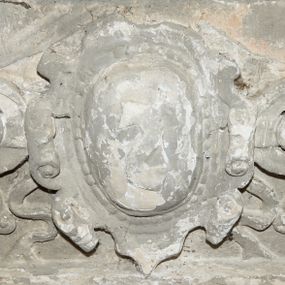 Zdjęcie nr 1: Fragment dekoracji wieńczącej nagrobek Joachima Lubomirskiego. W centrum kartusz z godłem herbu Drużyna zdobiony perełkowaniem i ornamentem rollwerkowym. Flankują go spływy wolutowe uzupełnione wstążkami. 