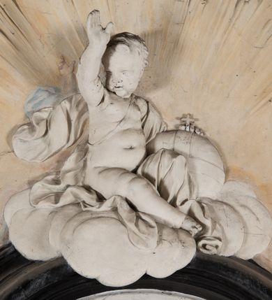 Zdjęcie nr 17: Na trójstopniowej podstawie osadzona prostopadłościenna mensa ołtarza ujęta lekko wybrzuszającymi się postumentami. Antepedium wykonane w technice marmoryzacji (skaliola) z owalnym polem pośrodku, z wyobrażeniem leżącego nagiego Dzieciątka Jezus z krzyżykiem w lewej dłoni i pierścieniem z krzyżem w prawej, pozostałe naroża wypełnione bukietami kwiatów. Na osi mensy nastawa w formie profilowanej ramy prostokątnej zamkniętej łukiem wklęsło-wypukłym, nadwieszonym, wypełnionej płaskorzeźbą z postacią św. Katarzyny. Święta ukazana w trzech czwartych, w pozycji klęczącej, na chmurach, z rękami złożonymi na piersi, z głową lekko odchyloną w głąb kompozycji. Jej twarz jest owalna, o pełnych policzkach, ze smukłym nosem, głębokimi oczodołami i otwartymi ustami. Na głowie włosy modelowane sumarycznie, długie, opadające na plecy oraz korona otwarta. Święta jest ubrana w długą suknię i obficie fałdowany płaszcz. Za jej plecami widoczny fragment koła – atrybutu jej męczeństwa, z przodu wyłaniające się płaskorzeźbione putta, z których jedno trzyma gałąź palmy. W górnej części kompozycji modelowane w płytkim reliefie chmury z widocznymi między nimi promieniami oraz uskrzydlone główki aniołków. Po bokach kolumny osadzone na bazach, ścięte w połowie wysokości ramy, zakończone skłębionymi obłokami chmur i siedzącymi na nich aniołkami. Lewy ukazany w pozycji półleżącej, z prawą ręką na piersi, a lewą wyciągniętą w kierunku osi ołtarza, z głową skierowaną w jego prawą stronę. Anioł po przeciwnej stronie siedzi na obłoku okrakiem i trzyma w ręku palmę męczeństwa. W tle obu aniołów płaskorzeźbione grupy puttów z banderolami z nieczytelnymi inskrypcjami. Nastawę wieńczy gloria promienista, której promienie wchodzą w partię okna, z siedzącą na obłokach postacią małego Jezusa z kulą ziemską przy boku i z prawą ręką uniesioną w geście błogosławieństwa, ubranego w rozwiany na plecach płaszcz. Kompozycję uzupełniają płaskorzeźbione grupy uskrzydlonych aniołków. Ołtarz z elementami czarnego i białego marmuru, barwnej marmoryzacji i białego, częściowo złoconego stiuku. 