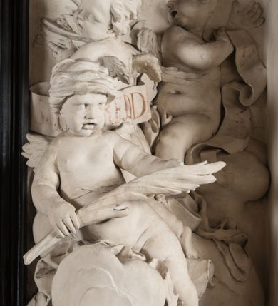 Zdjęcie nr 7: Na trójstopniowej podstawie osadzona prostopadłościenna mensa ołtarza ujęta lekko wybrzuszającymi się postumentami. Antepedium wykonane w technice marmoryzacji (skaliola) z owalnym polem pośrodku, z wyobrażeniem leżącego nagiego Dzieciątka Jezus z krzyżykiem w lewej dłoni i pierścieniem z krzyżem w prawej, pozostałe naroża wypełnione bukietami kwiatów. Na osi mensy nastawa w formie profilowanej ramy prostokątnej zamkniętej łukiem wklęsło-wypukłym, nadwieszonym, wypełnionej płaskorzeźbą z postacią św. Katarzyny. Święta ukazana w trzech czwartych, w pozycji klęczącej, na chmurach, z rękami złożonymi na piersi, z głową lekko odchyloną w głąb kompozycji. Jej twarz jest owalna, o pełnych policzkach, ze smukłym nosem, głębokimi oczodołami i otwartymi ustami. Na głowie włosy modelowane sumarycznie, długie, opadające na plecy oraz korona otwarta. Święta jest ubrana w długą suknię i obficie fałdowany płaszcz. Za jej plecami widoczny fragment koła – atrybutu jej męczeństwa, z przodu wyłaniające się płaskorzeźbione putta, z których jedno trzyma gałąź palmy. W górnej części kompozycji modelowane w płytkim reliefie chmury z widocznymi między nimi promieniami oraz uskrzydlone główki aniołków. Po bokach kolumny osadzone na bazach, ścięte w połowie wysokości ramy, zakończone skłębionymi obłokami chmur i siedzącymi na nich aniołkami. Lewy ukazany w pozycji półleżącej, z prawą ręką na piersi, a lewą wyciągniętą w kierunku osi ołtarza, z głową skierowaną w jego prawą stronę. Anioł po przeciwnej stronie siedzi na obłoku okrakiem i trzyma w ręku palmę męczeństwa. W tle obu aniołów płaskorzeźbione grupy puttów z banderolami z nieczytelnymi inskrypcjami. Nastawę wieńczy gloria promienista, której promienie wchodzą w partię okna, z siedzącą na obłokach postacią małego Jezusa z kulą ziemską przy boku i z prawą ręką uniesioną w geście błogosławieństwa, ubranego w rozwiany na plecach płaszcz. Kompozycję uzupełniają płaskorzeźbione grupy uskrzydlonych aniołków. Ołtarz z elementami czarnego i białego marmuru, barwnej marmoryzacji i białego, częściowo złoconego stiuku. 