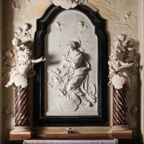 Zdjęcie nr 1: Na trójstopniowej podstawie osadzona prostopadłościenna mensa ołtarza ujęta lekko wybrzuszającymi się postumentami. Antepedium wykonane w technice marmoryzacji (skaliola) z owalnym polem pośrodku, z wyobrażeniem leżącego nagiego Dzieciątka Jezus z krzyżykiem w lewej dłoni i pierścieniem z krzyżem w prawej, pozostałe naroża wypełnione bukietami kwiatów. Na osi mensy nastawa w formie profilowanej ramy prostokątnej zamkniętej łukiem wklęsło-wypukłym, nadwieszonym, wypełnionej płaskorzeźbą z postacią św. Katarzyny. Święta ukazana w trzech czwartych, w pozycji klęczącej, na chmurach, z rękami złożonymi na piersi, z głową lekko odchyloną w głąb kompozycji. Jej twarz jest owalna, o pełnych policzkach, ze smukłym nosem, głębokimi oczodołami i otwartymi ustami. Na głowie włosy modelowane sumarycznie, długie, opadające na plecy oraz korona otwarta. Święta jest ubrana w długą suknię i obficie fałdowany płaszcz. Za jej plecami widoczny fragment koła – atrybutu jej męczeństwa, z przodu wyłaniające się płaskorzeźbione putta, z których jedno trzyma gałąź palmy. W górnej części kompozycji modelowane w płytkim reliefie chmury z widocznymi między nimi promieniami oraz uskrzydlone główki aniołków. Po bokach kolumny osadzone na bazach, ścięte w połowie wysokości ramy, zakończone skłębionymi obłokami chmur i siedzącymi na nich aniołkami. Lewy ukazany w pozycji półleżącej, z prawą ręką na piersi, a lewą wyciągniętą w kierunku osi ołtarza, z głową skierowaną w jego prawą stronę. Anioł po przeciwnej stronie siedzi na obłoku okrakiem i trzyma w ręku palmę męczeństwa. W tle obu aniołów płaskorzeźbione grupy puttów z banderolami z nieczytelnymi inskrypcjami. Nastawę wieńczy gloria promienista, której promienie wchodzą w partię okna, z siedzącą na obłokach postacią małego Jezusa z kulą ziemską przy boku i z prawą ręką uniesioną w geście błogosławieństwa, ubranego w rozwiany na plecach płaszcz. Kompozycję uzupełniają płaskorzeźbione grupy uskrzydlonych aniołków. Ołtarz z elementami czarnego i białego marmuru, barwnej marmoryzacji i białego, częściowo złoconego stiuku. 