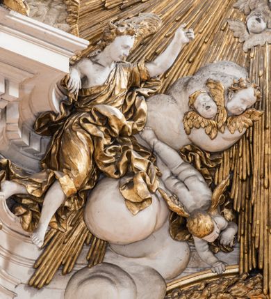 Zdjęcie nr 26: Zasadniczy ołtarz jest prostopadłościenny, z antepedium w technice skalioli, z owalnym polem, w którym znajduje się medalion obwiedziony kwiatami. Wydzielone wokół niego geometryczne pola pokryte są białą i czerwoną marmoryzacją. Za ołtarzem znajduje się monumentalna nastawa, składająca się z podwójnych cokołów, dwóch tylnych, ustawionych równolegle do prezbiterium, dwóch przednich ustawionych ukośnie, na których stoją osadzone na tle pilastrów kolumny o spiralnych trzonach. Po bokach kolumn unoszące się na chmurach uskrzydlone anioły w miękko modelowanych szatach. Trzony kolumn ozdobione wijącą się wokół nich wicią roślinną, ich kapitele w porządku kompozytowym podtrzymują belkowanie. Nad zewnętrznymi kolumnami unoszą się faliste naczółki, zaś nad wewnętrznymi siedzące anioły. Nad ołtarzem posadowiono dużych rozmiarów glorię promienistą z grupą aniołów i puttów. Pośrodku otwarta księga trzymana przez anioły z napisem: LIBER GENERATIONIS IESV CHRISTI. W polu środkowym nisza na obraz w kształcie prostokąta zamkniętego półkoliście, obwiedzionego rzeźbioną ramą z motywem liści lauru; na obrazie przedstawiona św. Anna Samotrzeć. Ołtarz flankują wsunięte do przodu figury św. Wojciecha i św. Stanisława, stojące na dostawionych do ścian bocznych prezbiterium cokołach, wybrzuszających się w górnej części. 