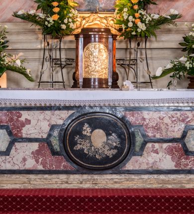 Zdjęcie nr 22: Zasadniczy ołtarz jest prostopadłościenny, z antepedium w technice skalioli, z owalnym polem, w którym znajduje się medalion obwiedziony kwiatami. Wydzielone wokół niego geometryczne pola pokryte są białą i czerwoną marmoryzacją. Za ołtarzem znajduje się monumentalna nastawa, składająca się z podwójnych cokołów, dwóch tylnych, ustawionych równolegle do prezbiterium, dwóch przednich ustawionych ukośnie, na których stoją osadzone na tle pilastrów kolumny o spiralnych trzonach. Po bokach kolumn unoszące się na chmurach uskrzydlone anioły w miękko modelowanych szatach. Trzony kolumn ozdobione wijącą się wokół nich wicią roślinną, ich kapitele w porządku kompozytowym podtrzymują belkowanie. Nad zewnętrznymi kolumnami unoszą się faliste naczółki, zaś nad wewnętrznymi siedzące anioły. Nad ołtarzem posadowiono dużych rozmiarów glorię promienistą z grupą aniołów i puttów. Pośrodku otwarta księga trzymana przez anioły z napisem: LIBER GENERATIONIS IESV CHRISTI. W polu środkowym nisza na obraz w kształcie prostokąta zamkniętego półkoliście, obwiedzionego rzeźbioną ramą z motywem liści lauru; na obrazie przedstawiona św. Anna Samotrzeć. Ołtarz flankują wsunięte do przodu figury św. Wojciecha i św. Stanisława, stojące na dostawionych do ścian bocznych prezbiterium cokołach, wybrzuszających się w górnej części. 