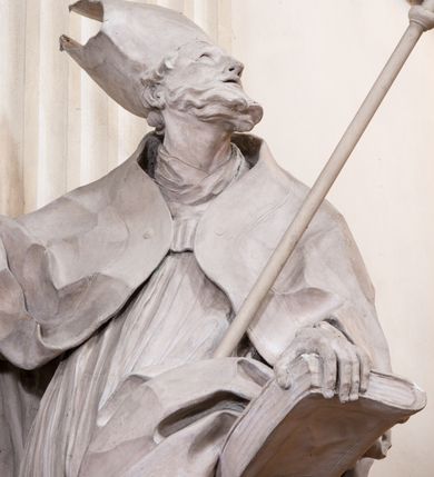 Zdjęcie nr 16: Zasadniczy ołtarz jest prostopadłościenny, z antepedium w technice skalioli, z owalnym polem, w którym znajduje się medalion obwiedziony kwiatami. Wydzielone wokół niego geometryczne pola pokryte są białą i czerwoną marmoryzacją. Za ołtarzem znajduje się monumentalna nastawa, składająca się z podwójnych cokołów, dwóch tylnych, ustawionych równolegle do prezbiterium, dwóch przednich ustawionych ukośnie, na których stoją osadzone na tle pilastrów kolumny o spiralnych trzonach. Po bokach kolumn unoszące się na chmurach uskrzydlone anioły w miękko modelowanych szatach. Trzony kolumn ozdobione wijącą się wokół nich wicią roślinną, ich kapitele w porządku kompozytowym podtrzymują belkowanie. Nad zewnętrznymi kolumnami unoszą się faliste naczółki, zaś nad wewnętrznymi siedzące anioły. Nad ołtarzem posadowiono dużych rozmiarów glorię promienistą z grupą aniołów i puttów. Pośrodku otwarta księga trzymana przez anioły z napisem: LIBER GENERATIONIS IESV CHRISTI. W polu środkowym nisza na obraz w kształcie prostokąta zamkniętego półkoliście, obwiedzionego rzeźbioną ramą z motywem liści lauru; na obrazie przedstawiona św. Anna Samotrzeć. Ołtarz flankują wsunięte do przodu figury św. Wojciecha i św. Stanisława, stojące na dostawionych do ścian bocznych prezbiterium cokołach, wybrzuszających się w górnej części. 