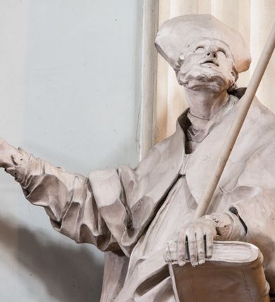 Zdjęcie nr 17: Zasadniczy ołtarz jest prostopadłościenny, z antepedium w technice skalioli, z owalnym polem, w którym znajduje się medalion obwiedziony kwiatami. Wydzielone wokół niego geometryczne pola pokryte są białą i czerwoną marmoryzacją. Za ołtarzem znajduje się monumentalna nastawa, składająca się z podwójnych cokołów, dwóch tylnych, ustawionych równolegle do prezbiterium, dwóch przednich ustawionych ukośnie, na których stoją osadzone na tle pilastrów kolumny o spiralnych trzonach. Po bokach kolumn unoszące się na chmurach uskrzydlone anioły w miękko modelowanych szatach. Trzony kolumn ozdobione wijącą się wokół nich wicią roślinną, ich kapitele w porządku kompozytowym podtrzymują belkowanie. Nad zewnętrznymi kolumnami unoszą się faliste naczółki, zaś nad wewnętrznymi siedzące anioły. Nad ołtarzem posadowiono dużych rozmiarów glorię promienistą z grupą aniołów i puttów. Pośrodku otwarta księga trzymana przez anioły z napisem: LIBER GENERATIONIS IESV CHRISTI. W polu środkowym nisza na obraz w kształcie prostokąta zamkniętego półkoliście, obwiedzionego rzeźbioną ramą z motywem liści lauru; na obrazie przedstawiona św. Anna Samotrzeć. Ołtarz flankują wsunięte do przodu figury św. Wojciecha i św. Stanisława, stojące na dostawionych do ścian bocznych prezbiterium cokołach, wybrzuszających się w górnej części. 