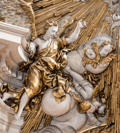 Zdjęcie nr 27: Zasadniczy ołtarz jest prostopadłościenny, z antepedium w technice skalioli, z owalnym polem, w którym znajduje się medalion obwiedziony kwiatami. Wydzielone wokół niego geometryczne pola pokryte są białą i czerwoną marmoryzacją. Za ołtarzem znajduje się monumentalna nastawa, składająca się z podwójnych cokołów, dwóch tylnych, ustawionych równolegle do prezbiterium, dwóch przednich ustawionych ukośnie, na których stoją osadzone na tle pilastrów kolumny o spiralnych trzonach. Po bokach kolumn unoszące się na chmurach uskrzydlone anioły w miękko modelowanych szatach. Trzony kolumn ozdobione wijącą się wokół nich wicią roślinną, ich kapitele w porządku kompozytowym podtrzymują belkowanie. Nad zewnętrznymi kolumnami unoszą się faliste naczółki, zaś nad wewnętrznymi siedzące anioły. Nad ołtarzem posadowiono dużych rozmiarów glorię promienistą z grupą aniołów i puttów. Pośrodku otwarta księga trzymana przez anioły z napisem: LIBER GENERATIONIS IESV CHRISTI. W polu środkowym nisza na obraz w kształcie prostokąta zamkniętego półkoliście, obwiedzionego rzeźbioną ramą z motywem liści lauru; na obrazie przedstawiona św. Anna Samotrzeć. Ołtarz flankują wsunięte do przodu figury św. Wojciecha i św. Stanisława, stojące na dostawionych do ścian bocznych prezbiterium cokołach, wybrzuszających się w górnej części. 