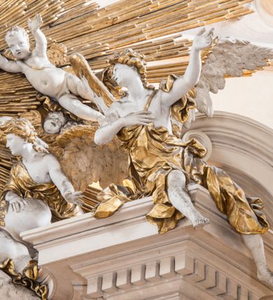 Zdjęcie nr 29: Zasadniczy ołtarz jest prostopadłościenny, z antepedium w technice skalioli, z owalnym polem, w którym znajduje się medalion obwiedziony kwiatami. Wydzielone wokół niego geometryczne pola pokryte są białą i czerwoną marmoryzacją. Za ołtarzem znajduje się monumentalna nastawa, składająca się z podwójnych cokołów, dwóch tylnych, ustawionych równolegle do prezbiterium, dwóch przednich ustawionych ukośnie, na których stoją osadzone na tle pilastrów kolumny o spiralnych trzonach. Po bokach kolumn unoszące się na chmurach uskrzydlone anioły w miękko modelowanych szatach. Trzony kolumn ozdobione wijącą się wokół nich wicią roślinną, ich kapitele w porządku kompozytowym podtrzymują belkowanie. Nad zewnętrznymi kolumnami unoszą się faliste naczółki, zaś nad wewnętrznymi siedzące anioły. Nad ołtarzem posadowiono dużych rozmiarów glorię promienistą z grupą aniołów i puttów. Pośrodku otwarta księga trzymana przez anioły z napisem: LIBER GENERATIONIS IESV CHRISTI. W polu środkowym nisza na obraz w kształcie prostokąta zamkniętego półkoliście, obwiedzionego rzeźbioną ramą z motywem liści lauru; na obrazie przedstawiona św. Anna Samotrzeć. Ołtarz flankują wsunięte do przodu figury św. Wojciecha i św. Stanisława, stojące na dostawionych do ścian bocznych prezbiterium cokołach, wybrzuszających się w górnej części. 