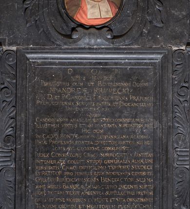Zdjęcie nr 4: Epitafium w formie stojącego prostokąta wsparte na profilowanym gzymsie z konsolami i podwieszonym pod nim fartuchem z kartuszem z herbem Uniwersytetu Jagiellońskiego, ujęte pilastrami podtrzymującymi przełamujący się w kwadrat gzyms, zwieńczony falistym, przerwanym przyczółkiem z krzyżem pośrodku. Pilastry z kapitelami w formie maszkaronów, trzymających w ustach kiść girland owocowych są ujęte od zewnątrz spływami wolutowymi, od wewnątrz ulistnionymi wydłużonymi wolutami. Pośrodku, w górnej wyłamanej części owalny portret zmarłego w kartuszu &quot;D(EO) O(PTIMO) M(AXIMO) PIIS MANIBUS / / PERILLUSTRIS OLIM ET REVERENDISSIMI DOMINI / M(AGISTRI) ANDREAE KRVPECKI / I(URIS) V(TRIUSQUE) D(OCTOR) ET P(HILOSOPHIAE) CANONICI CRACOVIENSIS PRAEPOSITI / PREMIICOVIENSIS SENIORIS PATRIS ET PROCANCELLARII / UNIVERSITATIS CRAC(OVIENSIS) / QUEM / CANDOR ANIMI AMABILEM ERUDITIO CONSPICUUM HONOR / ILLUSTREM VIRTUS ETIAM POST FATA SUPERSTITEM FECIT / HIC OLIM / IN CALVO MONTE. MOX IN LUBRANSCIANA ACADEMIA / PHI(LOSOPHI)AE PROFESSOR POSTEA DIRECTOR PARTEM SUI MELI/ORIS AEVI GLORIOSE CONSUMPSIT. / IUDEX CONSISTORII CRAC(OVIENSIS) SURROGATUS IUSTITIAM IN/ TEMERATE COLUIT, STUDII GENERALIS ALMAE UNI/VERSITATIS CRAC(OVIENSIS) DIFFICILIMO TEMPORE SEXDECI/ES RECTOR PRO IURIBUS EIUS INDEFESSUS CERTAVIT / COLLEGII IURIDICI INSIGNIS BENEFACTOR SED MAXIME HUIUS BASILICAE QUAM CUPRO INGENTI SU(M)PTU / PENE TOTAM TEXIT ARGENTEA SUPELLECTILI PRETIOSE / ORNAVIT IPSE MORIBUS COMITATE ET VITA ORNATISSIMUS / TANDEM DIERUM ET MERITORUM PLENUS CHRI/STIANE OBIIT ANNO SALUTIS 1.  7. 25 DIE 25 / APRILIS AETATIS SUAE 82. IN ECCLESIA CATHE/DRALIS CRACO(OVIENSIS) EXPECTAT. DONEC VENIAT IMMU/TATIO SUA IN HAC EIUS MEMORIAE HOC MONU/MENTUM EXECUTORES TESTAMENTI POSUERUNT&quot;.