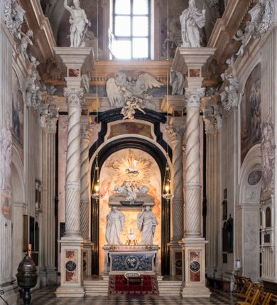 Zdjęcie nr 1: Na prostopadłościennej, wysokiej podstawie na kilkustopniowym podwyższeniu z dostawionym do niej ołtarzem, stoją personifikacje czterech Wydziałów Uniwersytetu – Teologii, Prawa, Medycyny i Sztuk Wyzwolonych, podtrzymujące trumnę z figurą putta w otoczeniu obłoków, które prawą ręką wskazuje na świętego, a lewą na posrebrzaną rzeźbę Baranka Apokaliptycznego na tle glorii i znajdującą poniżej banderolę z napisem: "Et lucerna eius est Agnus". Trumna ma kształt wybrzuszonego dołem sarkofagu z wiekiem ujętym dwiema wolutami. Ołtarz z antepedium wykonanym w technice skalioli z wyobrażeniem uskrzydlonego anioła trzymającego w rękach wieńce z kwiatów i lauru otoczonego witkami palm i rozlokowany i swobodnie pękami różnokolorowych kwiatków. Wokół grupy ustawiono cztery wolnostojące wysokie kolumny posadowione na wysokich postumentach, których ścianki są ozdobione czarnymi medalionami z motywami kwiatów wykonanymi w technice skalioli. Kolumny mają  skręcone trzony i kompozytowe kapitele, dźwigające odcinki belkowania, na których umieszczono figury czterech świętych Janów – Jana Chrzciciela, Jana Ewangelisty, Jana Kantego i Jana z Damaszku. 



