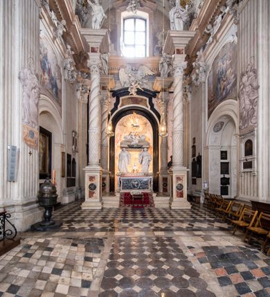 Zdjęcie nr 2: Na prostopadłościennej, wysokiej podstawie na kilkustopniowym podwyższeniu z dostawionym do niej ołtarzem, stoją personifikacje czterech Wydziałów Uniwersytetu – Teologii, Prawa, Medycyny i Sztuk Wyzwolonych, podtrzymujące trumnę z figurą putta w otoczeniu obłoków, które prawą ręką wskazuje na świętego, a lewą na posrebrzaną rzeźbę Baranka Apokaliptycznego na tle glorii i znajdującą poniżej banderolę z napisem: "Et lucerna eius est Agnus". Trumna ma kształt wybrzuszonego dołem sarkofagu z wiekiem ujętym dwiema wolutami. Ołtarz z antepedium wykonanym w technice skalioli z wyobrażeniem uskrzydlonego anioła trzymającego w rękach wieńce z kwiatów i lauru otoczonego witkami palm i rozlokowany i swobodnie pękami różnokolorowych kwiatków. Wokół grupy ustawiono cztery wolnostojące wysokie kolumny posadowione na wysokich postumentach, których ścianki są ozdobione czarnymi medalionami z motywami kwiatów wykonanymi w technice skalioli. Kolumny mają  skręcone trzony i kompozytowe kapitele, dźwigające odcinki belkowania, na których umieszczono figury czterech świętych Janów – Jana Chrzciciela, Jana Ewangelisty, Jana Kantego i Jana z Damaszku. 



