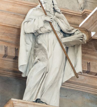 Zdjęcie nr 8: Na prostopadłościennej, wysokiej podstawie na kilkustopniowym podwyższeniu z dostawionym do niej ołtarzem, stoją personifikacje czterech Wydziałów Uniwersytetu – Teologii, Prawa, Medycyny i Sztuk Wyzwolonych, podtrzymujące trumnę z figurą putta w otoczeniu obłoków, które prawą ręką wskazuje na świętego, a lewą na posrebrzaną rzeźbę Baranka Apokaliptycznego na tle glorii i znajdującą poniżej banderolę z napisem: &quot;Et lucerna eius est Agnus&quot;. Trumna ma kształt wybrzuszonego dołem sarkofagu z wiekiem ujętym dwiema wolutami. Ołtarz z antepedium wykonanym w technice skalioli z wyobrażeniem uskrzydlonego anioła trzymającego w rękach wieńce z kwiatów i lauru otoczonego witkami palm i rozlokowany i swobodnie pękami różnokolorowych kwiatków. Wokół grupy ustawiono cztery wolnostojące wysokie kolumny posadowione na wysokich postumentach, których ścianki są ozdobione czarnymi medalionami z motywami kwiatów wykonanymi w technice skalioli. Kolumny mają  skręcone trzony i kompozytowe kapitele, dźwigające odcinki belkowania, na których umieszczono figury czterech świętych Janów – Jana Chrzciciela, Jana Ewangelisty, Jana Kantego i Jana z Damaszku. 



