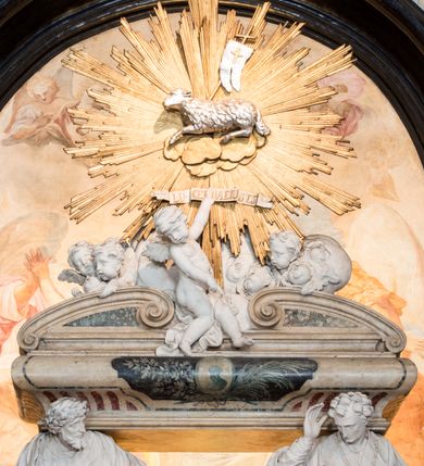 Zdjęcie nr 20: Na prostopadłościennej, wysokiej podstawie na kilkustopniowym podwyższeniu z dostawionym do niej ołtarzem, stoją personifikacje czterech Wydziałów Uniwersytetu – Teologii, Prawa, Medycyny i Sztuk Wyzwolonych, podtrzymujące trumnę z figurą putta w otoczeniu obłoków, które prawą ręką wskazuje na świętego, a lewą na posrebrzaną rzeźbę Baranka Apokaliptycznego na tle glorii i znajdującą poniżej banderolę z napisem: "Et lucerna eius est Agnus". Trumna ma kształt wybrzuszonego dołem sarkofagu z wiekiem ujętym dwiema wolutami. Ołtarz z antepedium wykonanym w technice skalioli z wyobrażeniem uskrzydlonego anioła trzymającego w rękach wieńce z kwiatów i lauru otoczonego witkami palm i rozlokowany i swobodnie pękami różnokolorowych kwiatków. Wokół grupy ustawiono cztery wolnostojące wysokie kolumny posadowione na wysokich postumentach, których ścianki są ozdobione czarnymi medalionami z motywami kwiatów wykonanymi w technice skalioli. Kolumny mają  skręcone trzony i kompozytowe kapitele, dźwigające odcinki belkowania, na których umieszczono figury czterech świętych Janów – Jana Chrzciciela, Jana Ewangelisty, Jana Kantego i Jana z Damaszku. 



