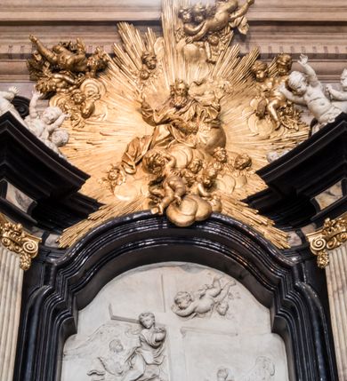 Zdjęcie nr 13: Ołtarz ustawiony na trójstopniowym podeście, prostopadłościenny, z antepedium z dekoracją w technice skaliola z pól geometrycznych dzielonych listwami i wypełniony drobnymi, wielobarwnymi kwiatkami. Za ołtarzem monumentalna nastawa utworzona z pilastrów i ukośnie ustawionych filarów stojących na wysokich postumentach. Ich trzony są kanelowane, a kapitele utworzone z jońskich wolut i przewiązanych taśmą lilijek. Nad kapitelami wznosi się belkowanie, nad zewnętrznymi pilastrami zwieńczone falistymi naczółkami, nad wewnętrznymi grupami uskrzydlonych puttów. Pośrodku znajduje się prostokątna wnęka zakończona łukiem półkolistym, nadwieszonym, w profilowanej ramie. W niej stiukowy relief przedstawiający Chwałę Krzyża Świętego adorowanego przez Matkę Boską z martwym Chrystusem spoczywającym na jej kolanach oraz przez św. Jana Ewangelistę odwróconego do widza plecami. Maria ukazana frontalnie, ubrana w rozłożystą suknię i  płaszcz zarzucony na głowę, z prawą ręką dotykająca głowy Jezusa, z lewą wyciągniętą do przodu. Jan przedstawiony w wykroku, z rękami wysuniętymi przed siebie, ubrany w suknię i płaszcz odkrywający lewy bark. Za Chrystusem ukazany anioł trzymający jego rękę. Nad nimi grupa aniołów unoszących krzyż. Ponad wnęką widnieje promienista, złocona gloria, z postacią Boga Ojca zasiadającego w chmurach, z gołębicą Ducha Świętego, puttami i główkami aniołów. Po bokach stoją figury św. Weroniki i św. Longina. Święta jest ubrana w długą, ekspresyjnie marszczoną suknię, w rękach trzyma rozłożoną chustę z twarzą Chrystusa. Longin jest przestawiony w zbroi rzymskiego legionisty, z długim, efektownie formowanym płaszczem, z lanca w prawej dłoni. 
