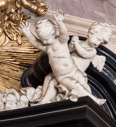 Zdjęcie nr 18: Ołtarz ustawiony na trójstopniowym podeście, prostopadłościenny, z antepedium z dekoracją w technice skaliola z pól geometrycznych dzielonych listwami i wypełniony drobnymi, wielobarwnymi kwiatkami. Za ołtarzem monumentalna nastawa utworzona z pilastrów i ukośnie ustawionych filarów stojących na wysokich postumentach. Ich trzony są kanelowane, a kapitele utworzone z jońskich wolut i przewiązanych taśmą lilijek. Nad kapitelami wznosi się belkowanie, nad zewnętrznymi pilastrami zwieńczone falistymi naczółkami, nad wewnętrznymi grupami uskrzydlonych puttów. Pośrodku znajduje się prostokątna wnęka zakończona łukiem półkolistym, nadwieszonym, w profilowanej ramie. W niej stiukowy relief przedstawiający Chwałę Krzyża Świętego adorowanego przez Matkę Boską z martwym Chrystusem spoczywającym na jej kolanach oraz przez św. Jana Ewangelistę odwróconego do widza plecami. Maria ukazana frontalnie, ubrana w rozłożystą suknię i  płaszcz zarzucony na głowę, z prawą ręką dotykająca głowy Jezusa, z lewą wyciągniętą do przodu. Jan przedstawiony w wykroku, z rękami wysuniętymi przed siebie, ubrany w suknię i płaszcz odkrywający lewy bark. Za Chrystusem ukazany anioł trzymający jego rękę. Nad nimi grupa aniołów unoszących krzyż. Ponad wnęką widnieje promienista, złocona gloria, z postacią Boga Ojca zasiadającego w chmurach, z gołębicą Ducha Świętego, puttami i główkami aniołów. Po bokach stoją figury św. Weroniki i św. Longina. Święta jest ubrana w długą, ekspresyjnie marszczoną suknię, w rękach trzyma rozłożoną chustę z twarzą Chrystusa. Longin jest przestawiony w zbroi rzymskiego legionisty, z długim, efektownie formowanym płaszczem, z lanca w prawej dłoni. 
