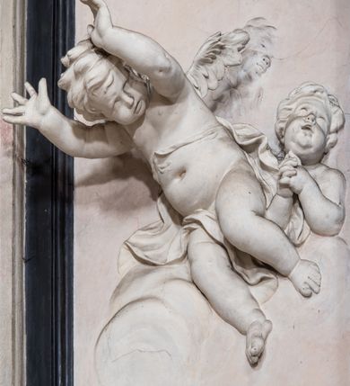 Zdjęcie nr 14: Ołtarz ustawiony na trójstopniowym podeście, prostopadłościenny, z antepedium z dekoracją w technice skaliola z pól geometrycznych dzielonych listwami i wypełniony drobnymi, wielobarwnymi kwiatkami. Za ołtarzem monumentalna nastawa utworzona z pilastrów i ukośnie ustawionych filarów stojących na wysokich postumentach. Ich trzony są kanelowane, a kapitele utworzone z jońskich wolut i przewiązanych taśmą lilijek. Nad kapitelami wznosi się belkowanie, nad zewnętrznymi pilastrami zwieńczone falistymi naczółkami, nad wewnętrznymi grupami uskrzydlonych puttów. Pośrodku znajduje się prostokątna wnęka zakończona łukiem półkolistym, nadwieszonym, w profilowanej ramie. W niej stiukowy relief przedstawiający Chwałę Krzyża Świętego adorowanego przez Matkę Boską z martwym Chrystusem spoczywającym na jej kolanach oraz przez św. Jana Ewangelistę odwróconego do widza plecami. Maria ukazana frontalnie, ubrana w rozłożystą suknię i  płaszcz zarzucony na głowę, z prawą ręką dotykająca głowy Jezusa, z lewą wyciągniętą do przodu. Jan przedstawiony w wykroku, z rękami wysuniętymi przed siebie, ubrany w suknię i płaszcz odkrywający lewy bark. Za Chrystusem ukazany anioł trzymający jego rękę. Nad nimi grupa aniołów unoszących krzyż. Ponad wnęką widnieje promienista, złocona gloria, z postacią Boga Ojca zasiadającego w chmurach, z gołębicą Ducha Świętego, puttami i główkami aniołów. Po bokach stoją figury św. Weroniki i św. Longina. Święta jest ubrana w długą, ekspresyjnie marszczoną suknię, w rękach trzyma rozłożoną chustę z twarzą Chrystusa. Longin jest przestawiony w zbroi rzymskiego legionisty, z długim, efektownie formowanym płaszczem, z lanca w prawej dłoni. 
