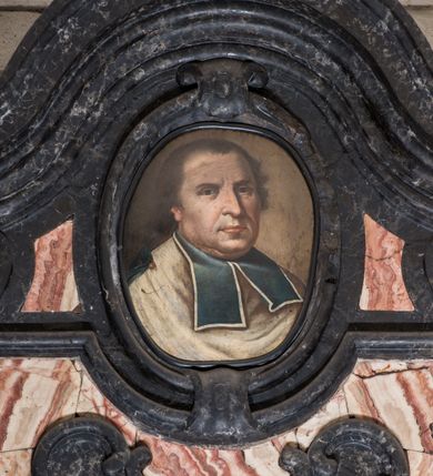 Zdjęcie nr 2: Epitafium w kształcie pionowej tablicy, ujętej spływami wolutowymi z kampanulami, z owalnym polem na portret, zwieńczonej profilowanym, falistym gzymsem. U dołu kartusz z herbem Prus III pod kapeluszem kanonickim zwieńczony muszlą. Portret ujęty profilowaniem z dwiema taśmami, przedstawia mężczyznę w popiersiu, w białym kołnierzu z turkusowymi befkami, z głową ukazaną w trzech czwartych, zwróconą lekko w lewo. Jego twarz jest pełna, nos wydatny, prosty, oczy otwarte, spoglądają wprost, usta zamknięte, wyraziście zaznaczone czerwienią, włosy krótkie, kręcone na bokach, odsłaniające niewielkie zakola. Tło nieokreślone, w tonacji brązów. Tablica z inskrypcją prostokątna, o zaoblonych, ujętych ceownicami narożach i wyciętych niemal półkoliście krótszych bokach, w niej złocona inskrypcja: &quot;D(EO) O(PTIMO) M(AXIMO) / IOANNI IOSEPHO / RYGALSKI /  SACRAE THEOLOGIAE DOCTRO I PROFESSORI / ECCLESIAE COLLEGIATAE SANCTI FLORIANI CUSTODI / UNIVERSITATIS ALMAE / FILIO PATRI RECTORI / SAPIENTI MUNIFICIO MORIGERO / CARO MAGNIFICO / QUI TURRES ISTIUS TEMPLI AERE PANNONIO/ TECTAS ASTRIS INTULIT. / COLLEGIATAS et PAROCHIALEM VETERO CORCINENSEM / QUAS REXIT et ORNAVIT ECCLESIAS / SACRA SUPELLECTILI DITAVIT. / ANNO SALUTIS GENERIS HUMANI MDCCLXXIX / AETATIS LXI / VIAM UNIVERSAE CARNIS INGRESSO / FIDI DOLENTES EXECUTORES / AMORIS MEMORIAE ERGO / POSUERE / Quid Solutis est Beatius curis / Cum mensonus reponit ac peregrino / Labore fessi venimus Patriam ad nostram / Hoc est quod unum est pio laboribus antis!&quot;. 